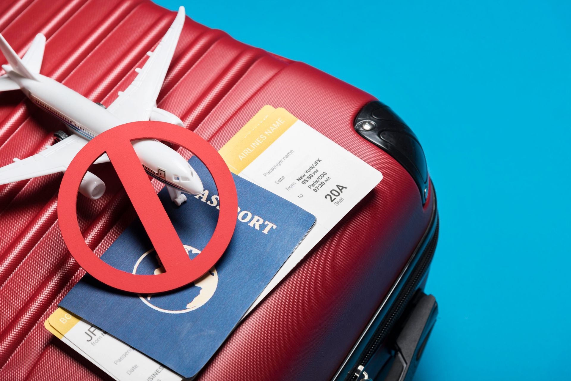 A red suitcase with a model airplane , passport , and ticket on it.
