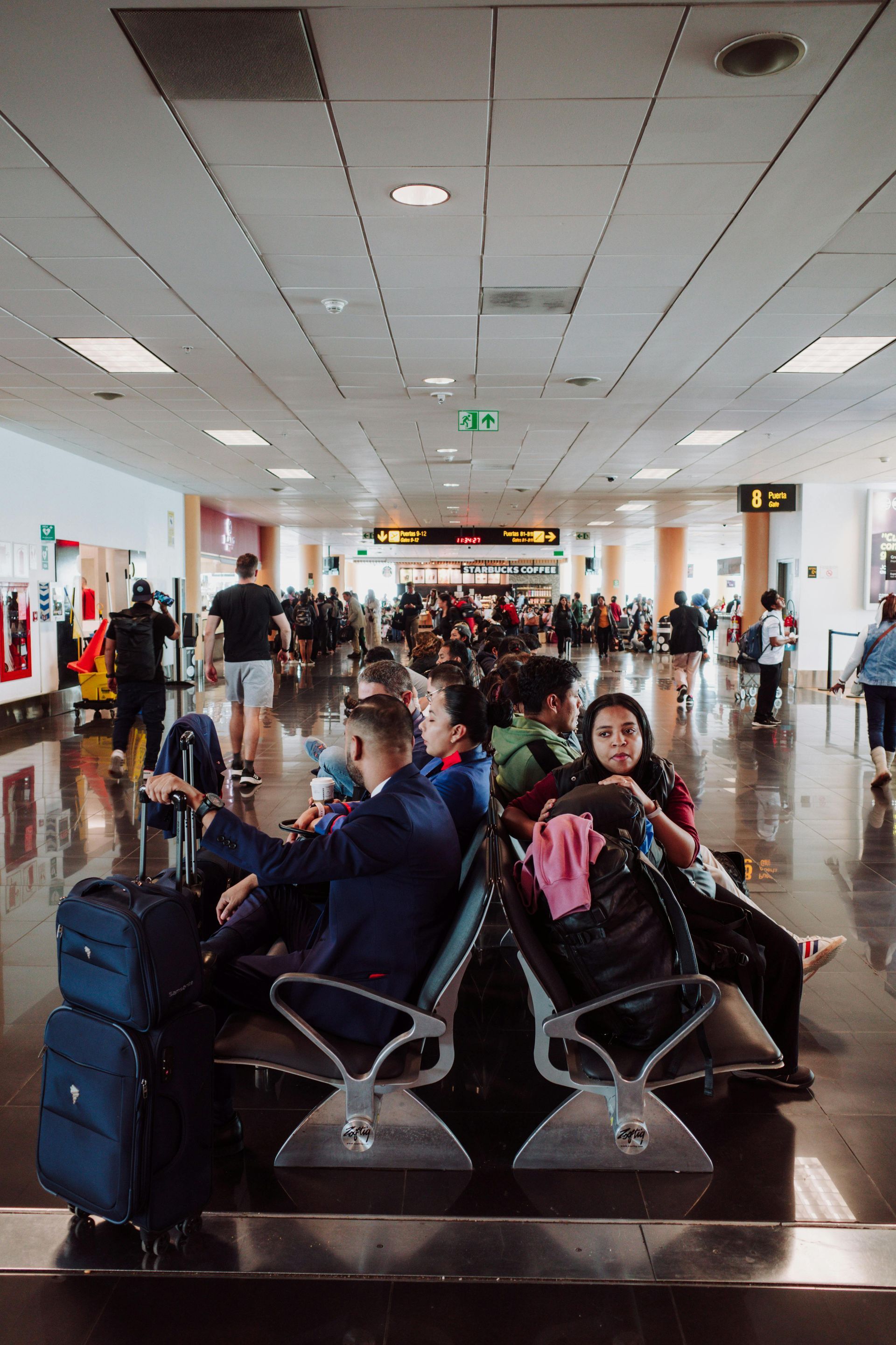 A group of people are sitting in chairs at an airport waiting area.
