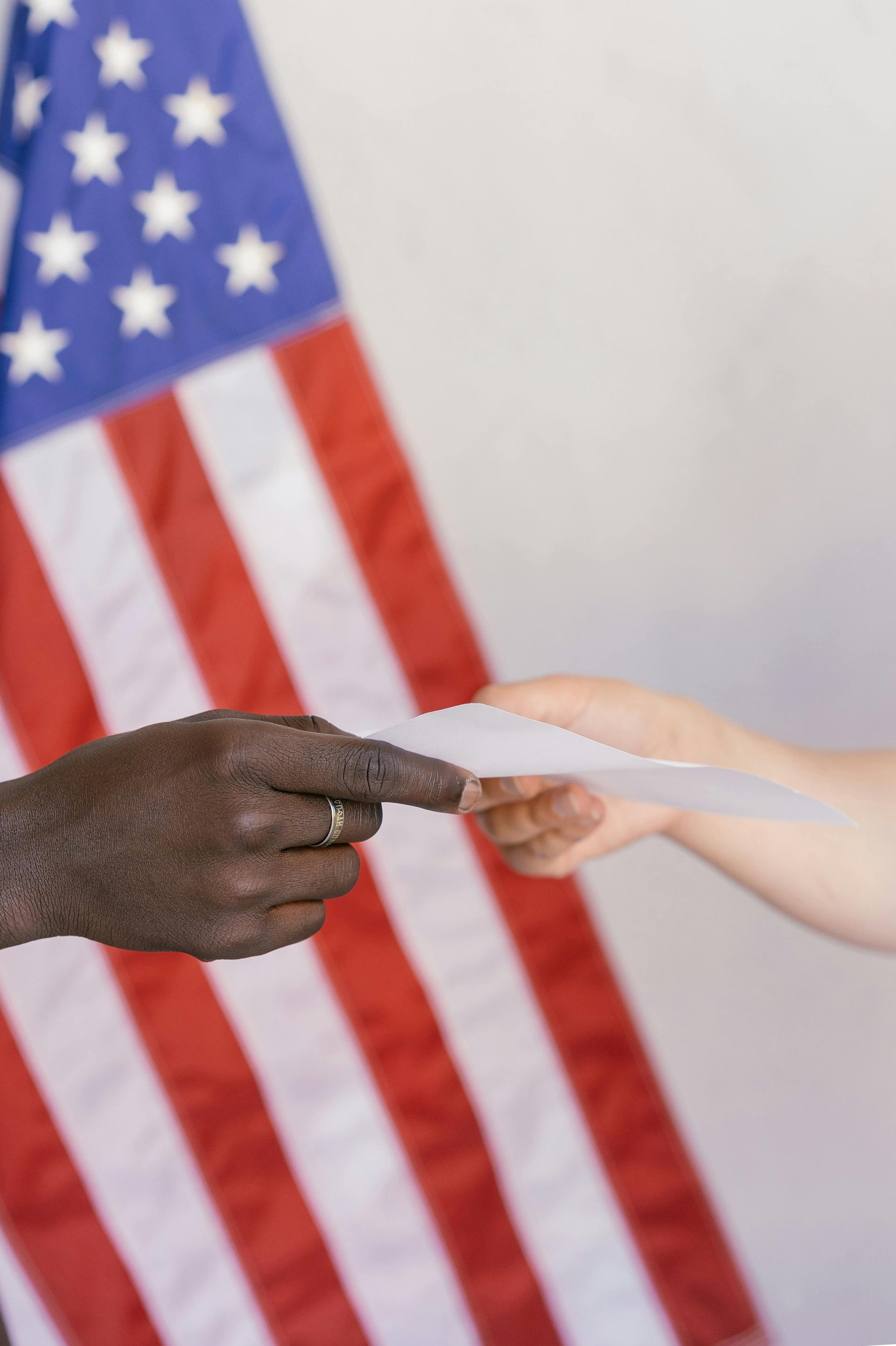 A person is handing a piece of paper to another person in front of an american flag.