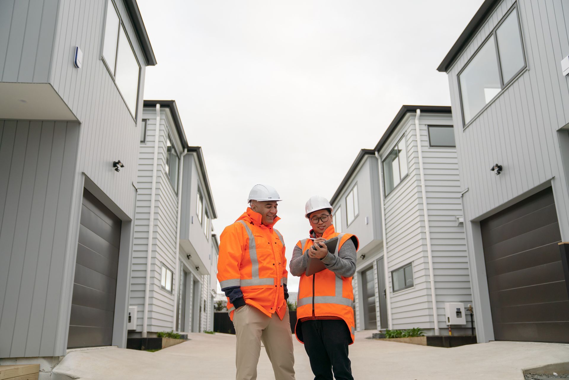 Two construction workers are standing in front of a row of houses.