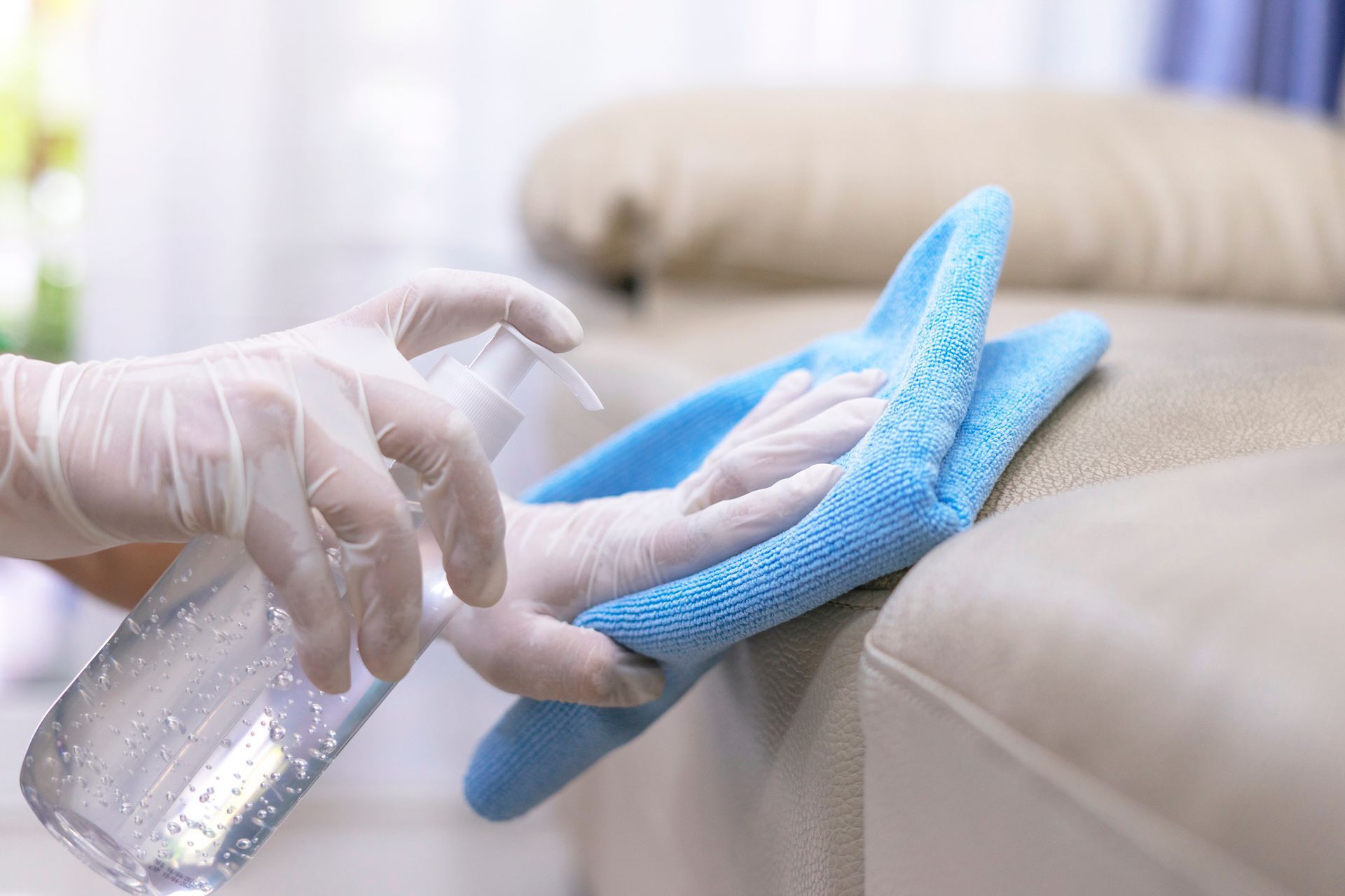 A person is cleaning a couch with a cloth and a spray bottle.