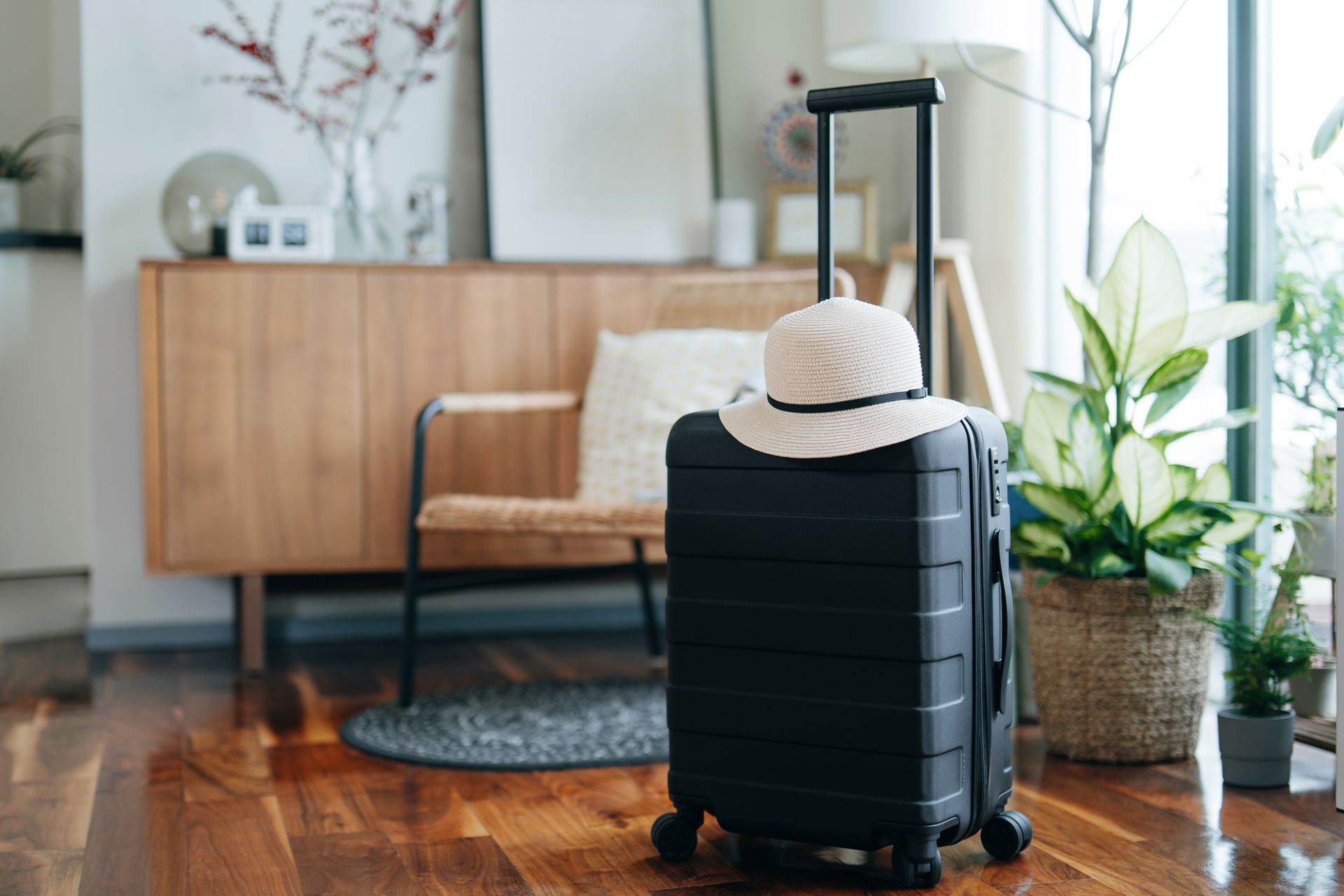 A black suitcase with a hat on top of it is sitting on a wooden floor in a living room.