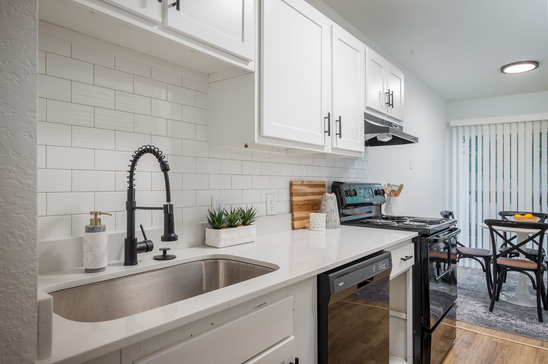 White kitchen with subway tile backsplash, stainless steel sink, black faucet, and appliances.