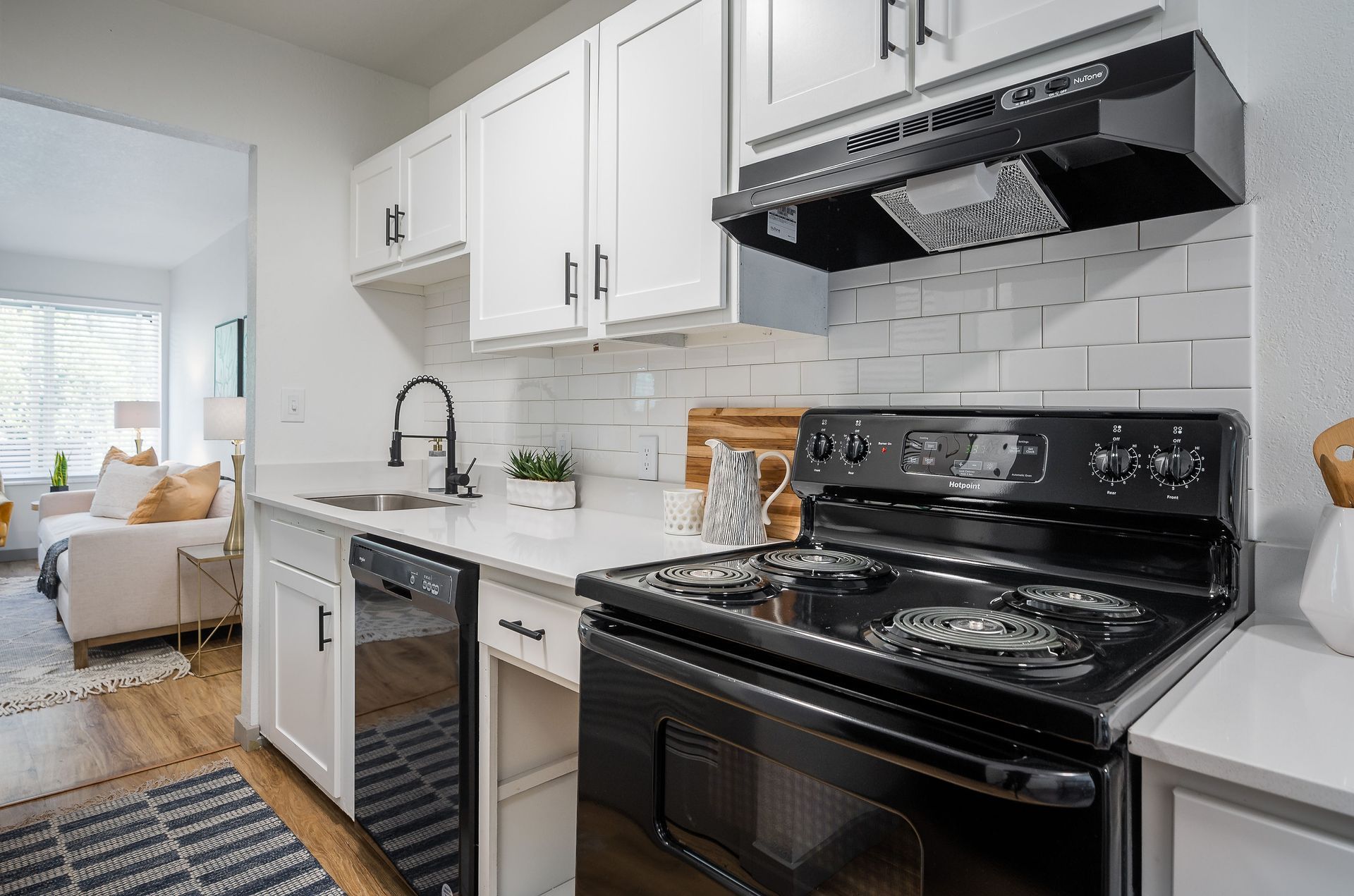 White kitchen with black appliances, white subway tile backsplash, and a glimpse of a living room.