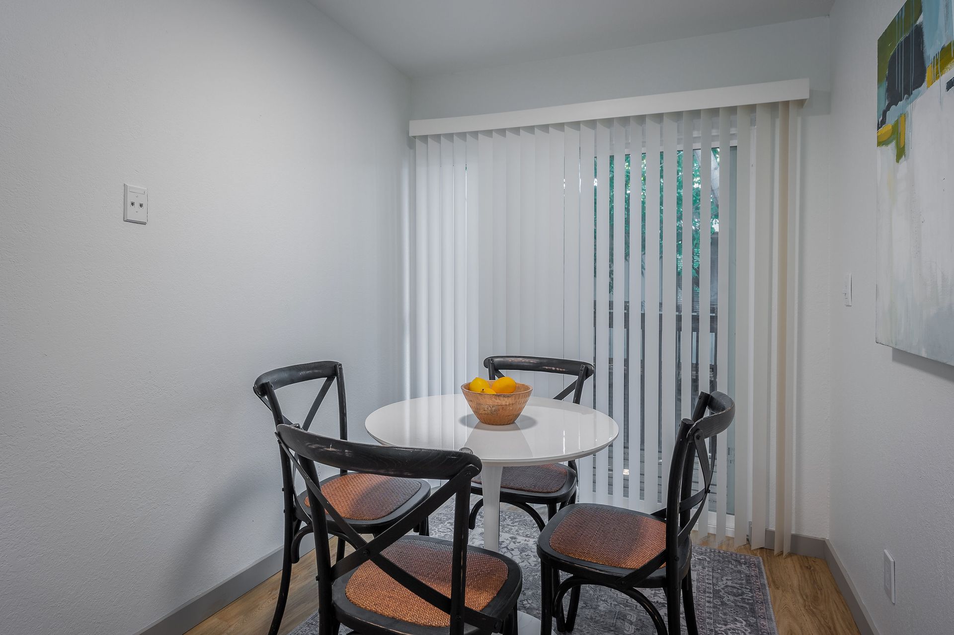 Dining area with white table, four chairs, and sliding door with vertical blinds.