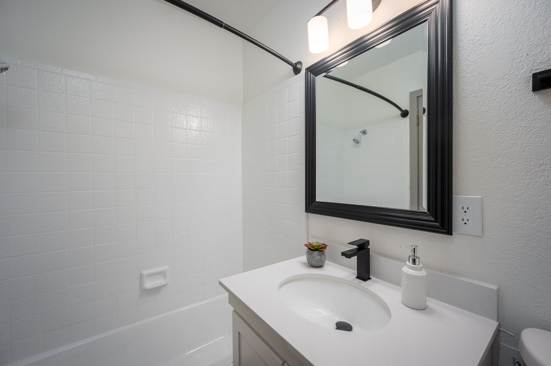 Bathroom with white tile shower, vanity with black faucet, and large mirror.