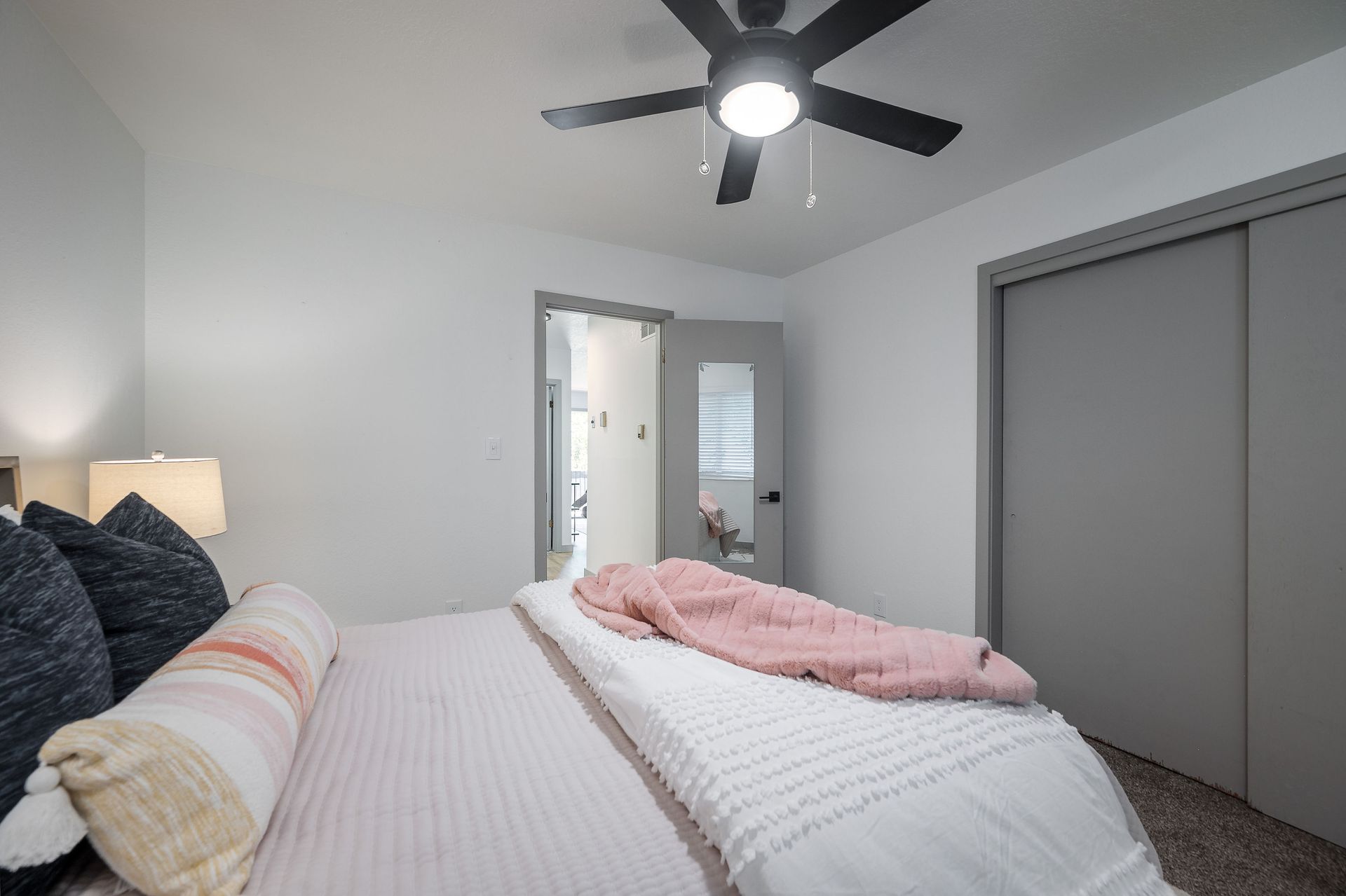 Bedroom with bed, closet, doorway, and ceiling fan. Pink and white bedding with gray walls.