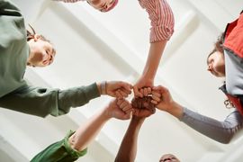 Hands stacked together in a team huddle against a bright indoor ceiling