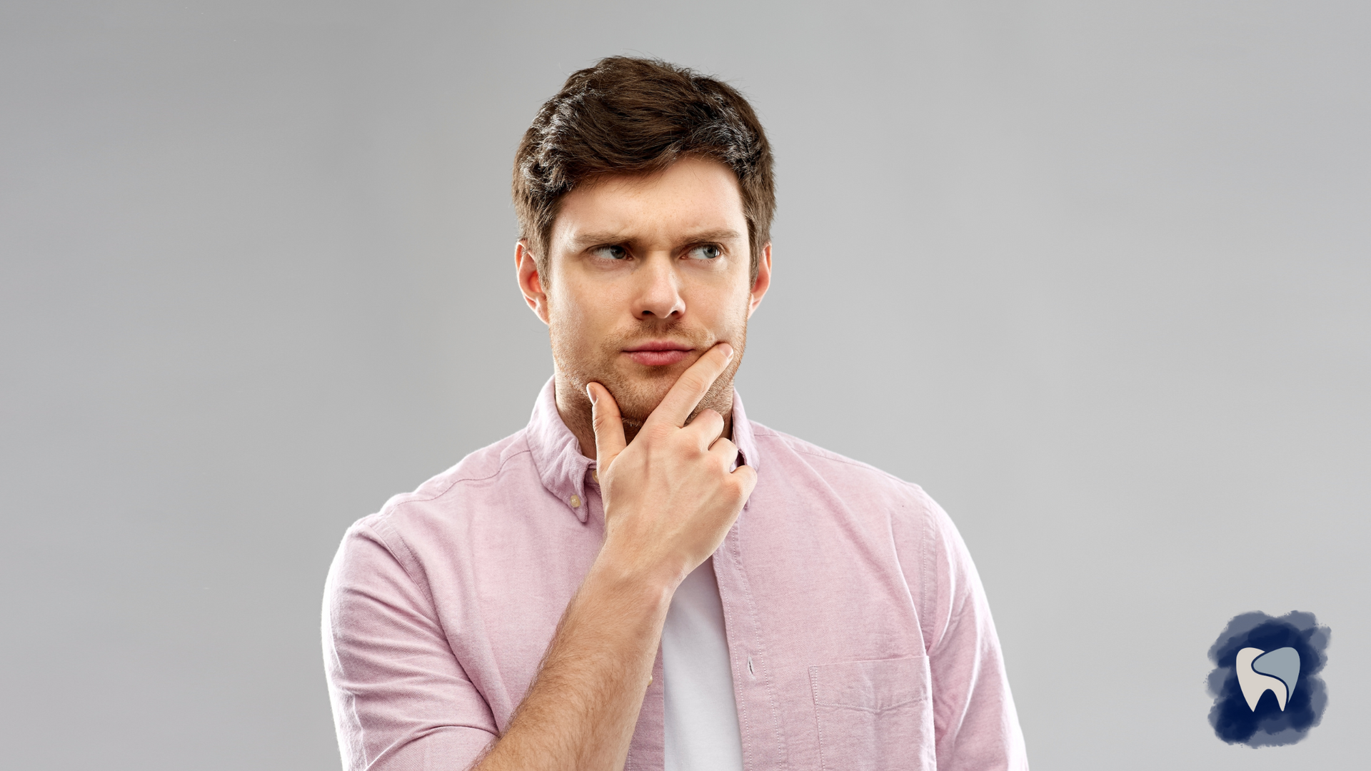 Man in pink shirt, hand on chin, appears thoughtful, looking up. Gray background.