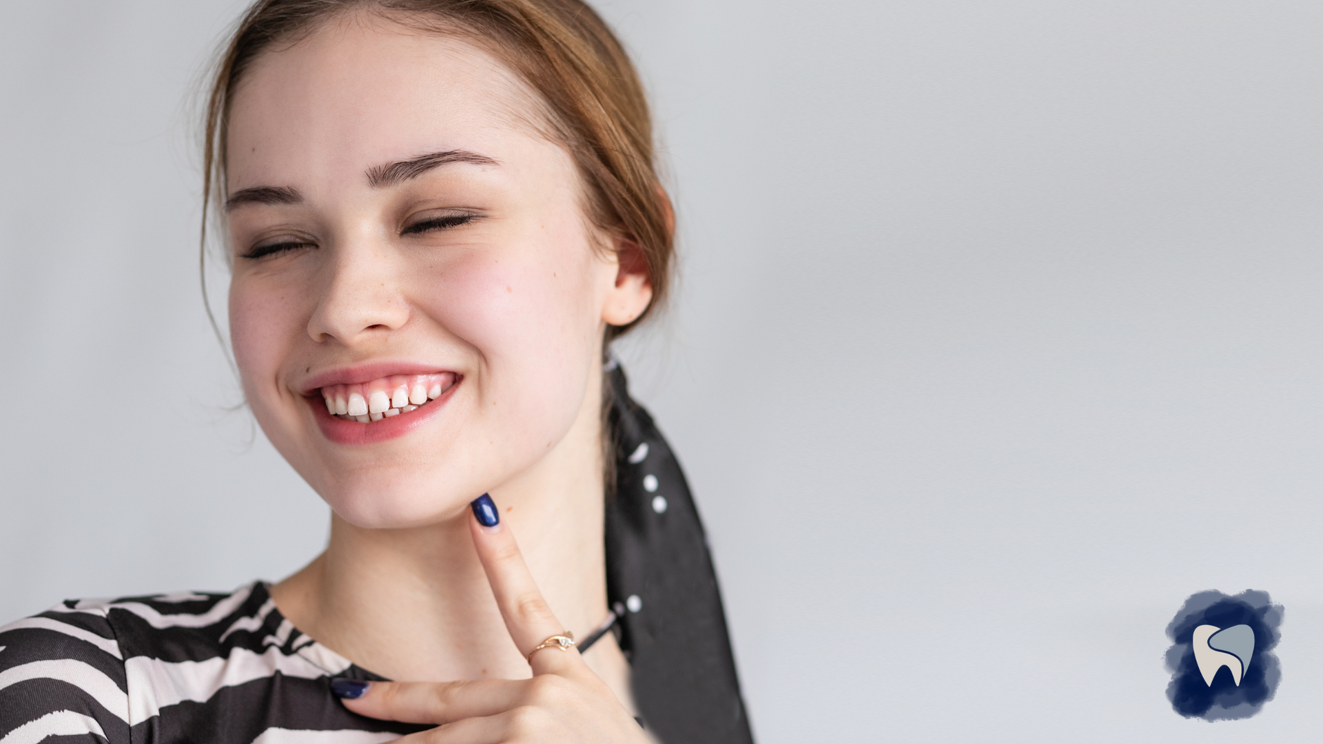 Woman smiling, pointing to her jaw; black and white striped top, light background.