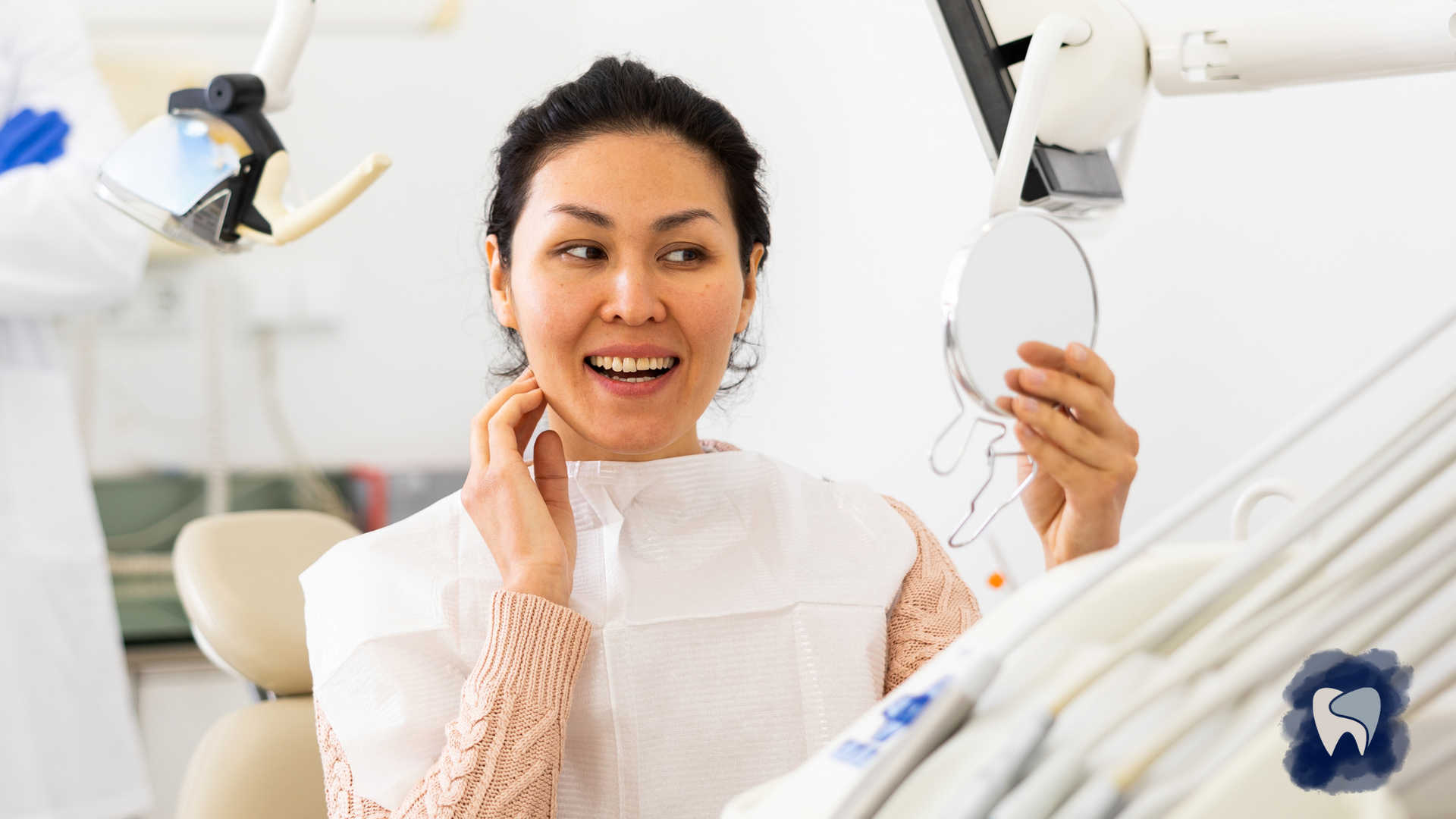 Woman in dental chair smiles while holding a mirror, examining her teeth after a procedure.