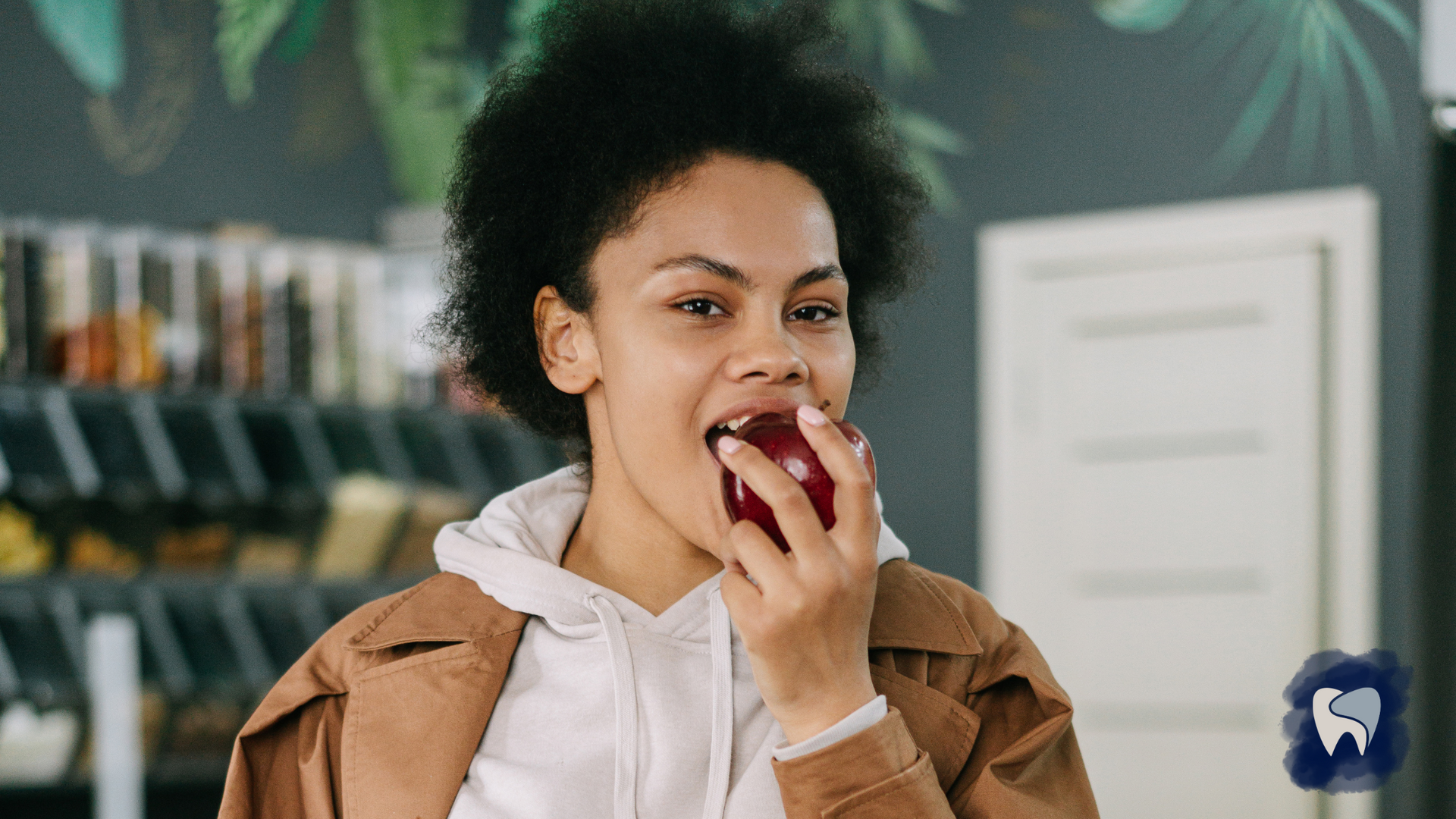 Woman bites into red apple in a grocery store setting, smiling.