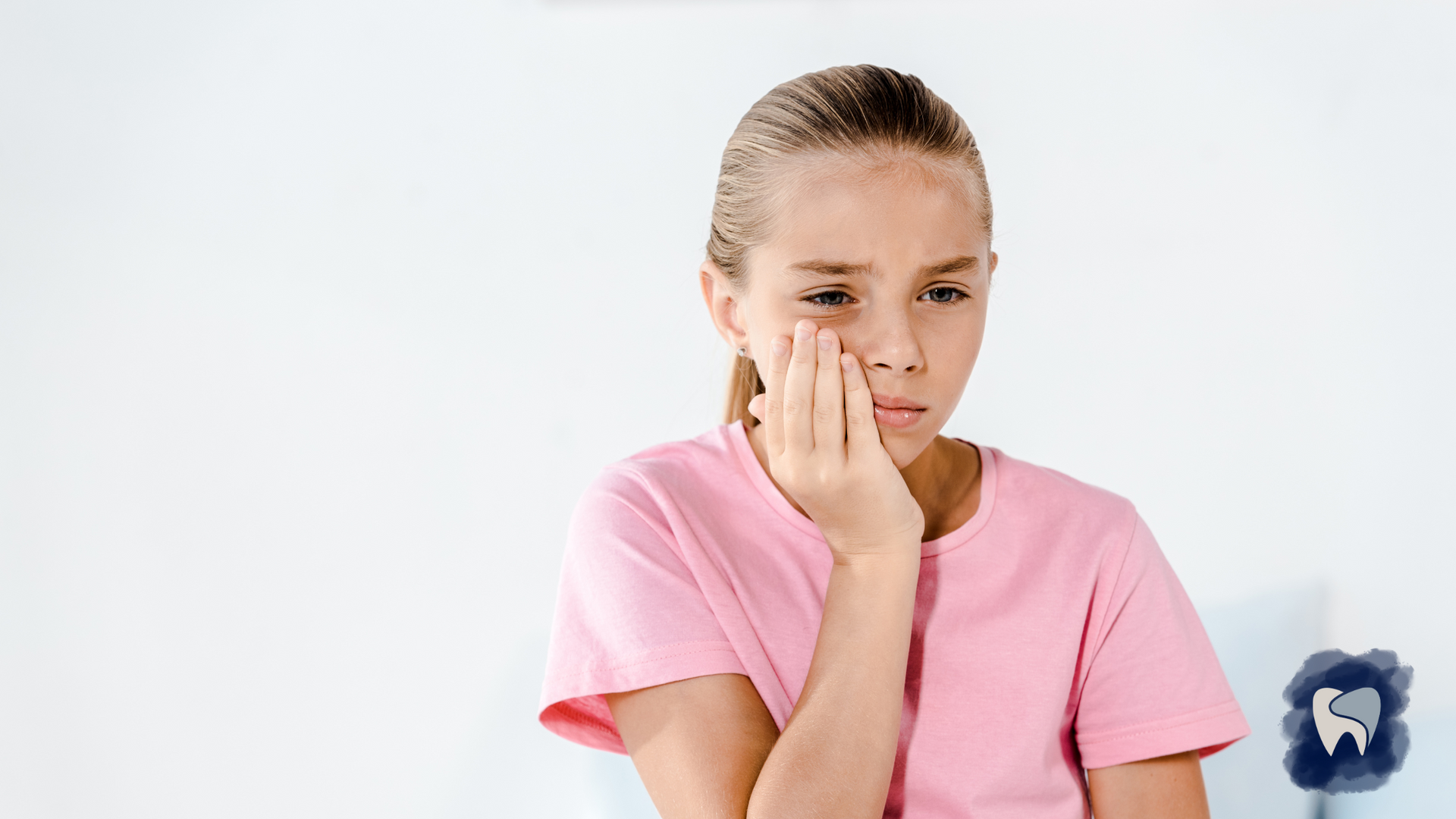Girl in pink shirt holding her cheek, appearing to have a toothache.