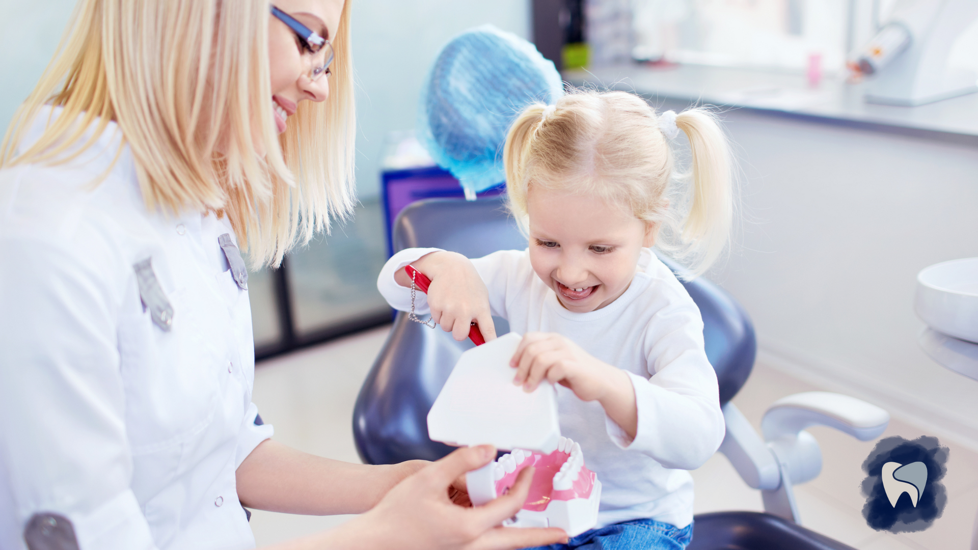 Dentist showing a young child a model of teeth, child smiles while holding a tool, dental office.