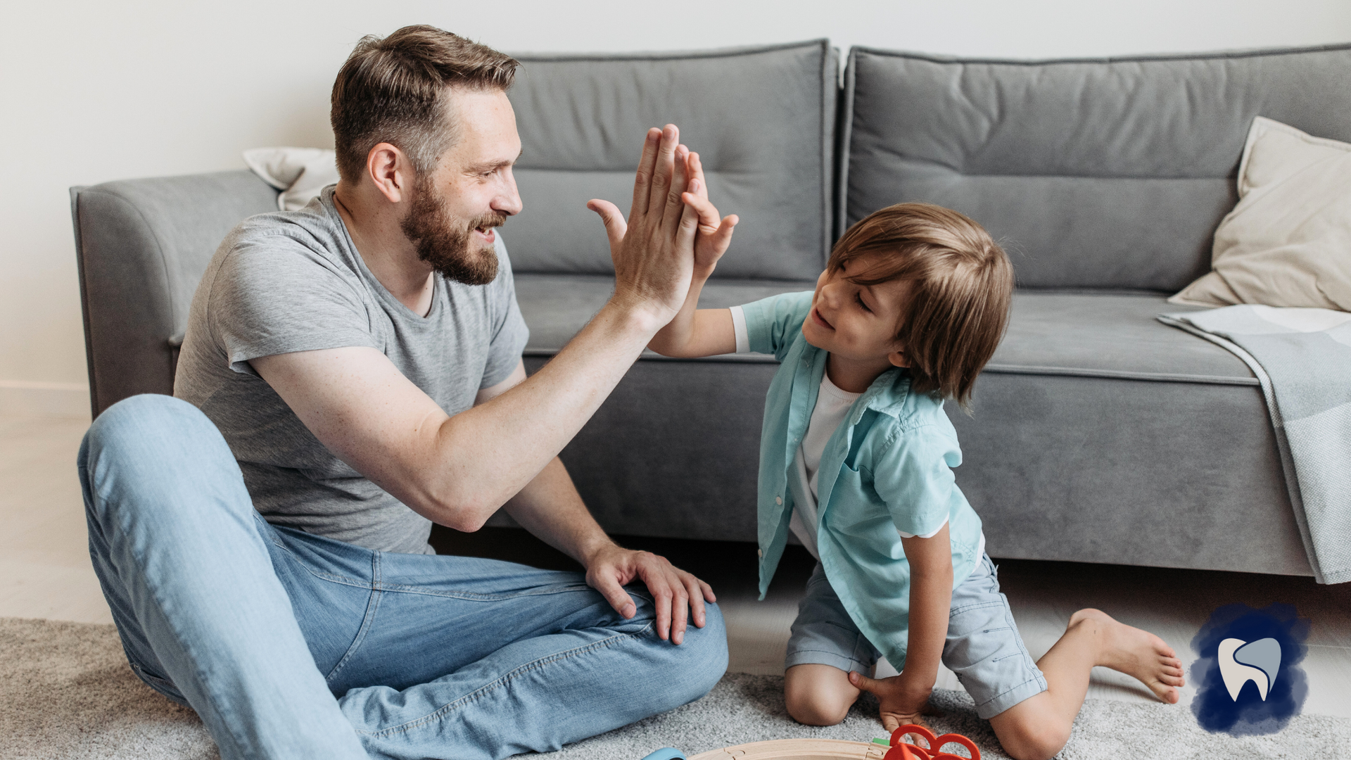 Man and child high-five on a rug in front of a gray couch. Both are smiling.