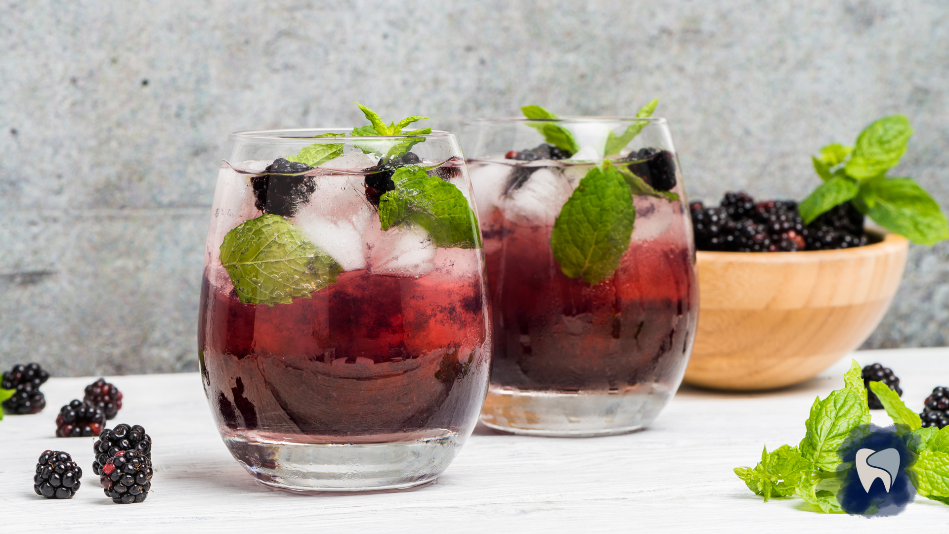 Two blackberry mojitos with mint and ice, next to a bowl of blackberries and mint sprigs.