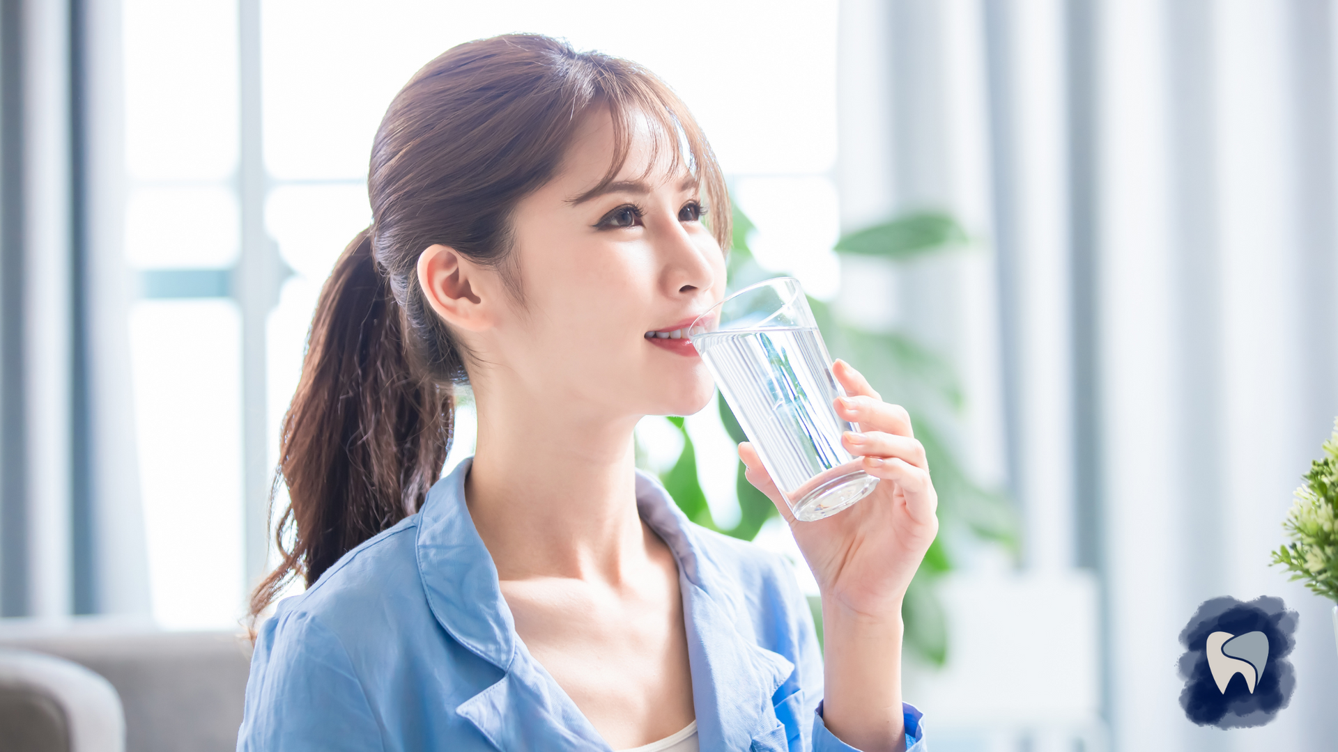 Woman drinking water from a glass; sunny indoor setting.
