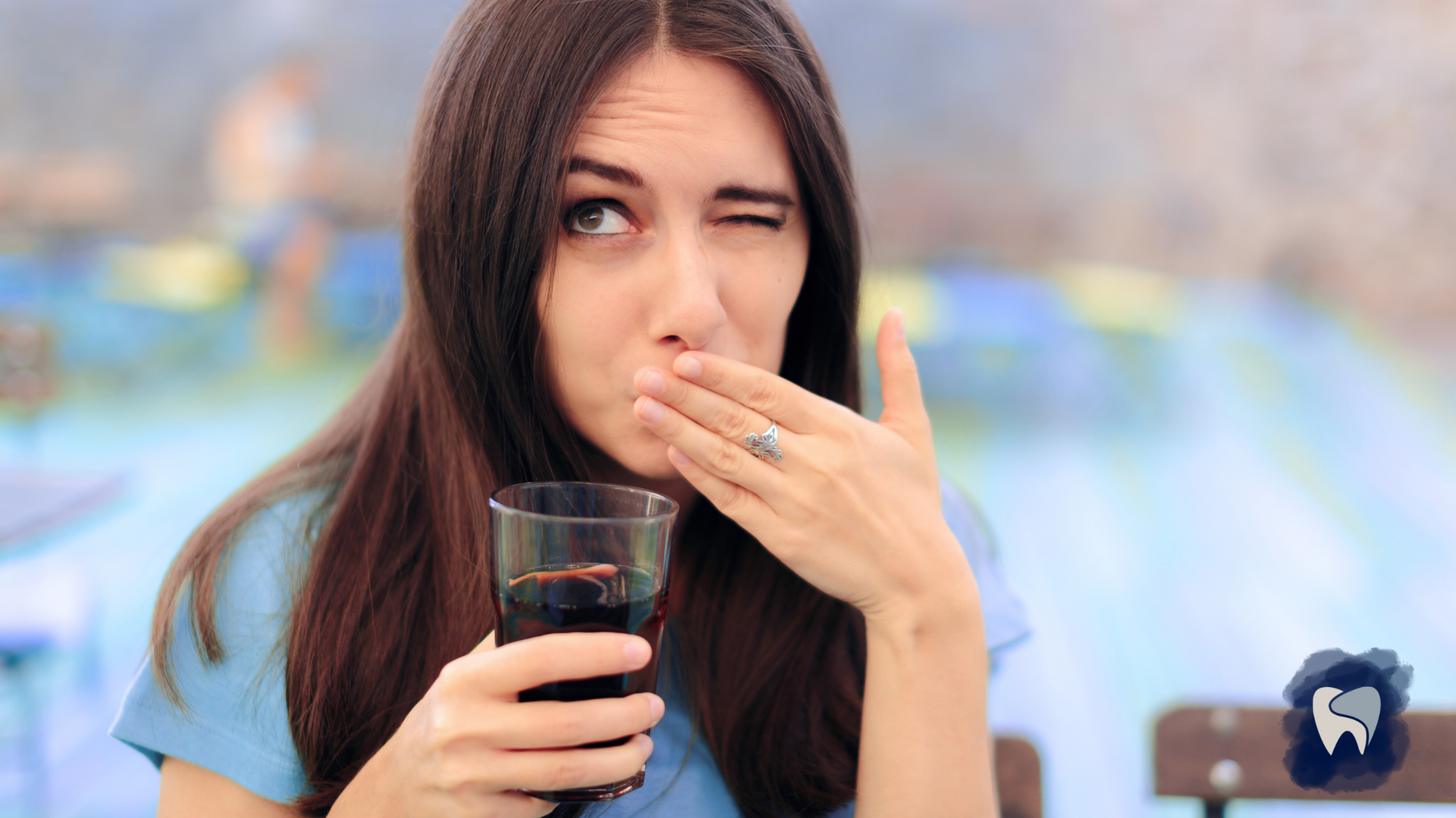 Woman with drink, making a face as if something tastes bad, winking and holding hand near mouth.