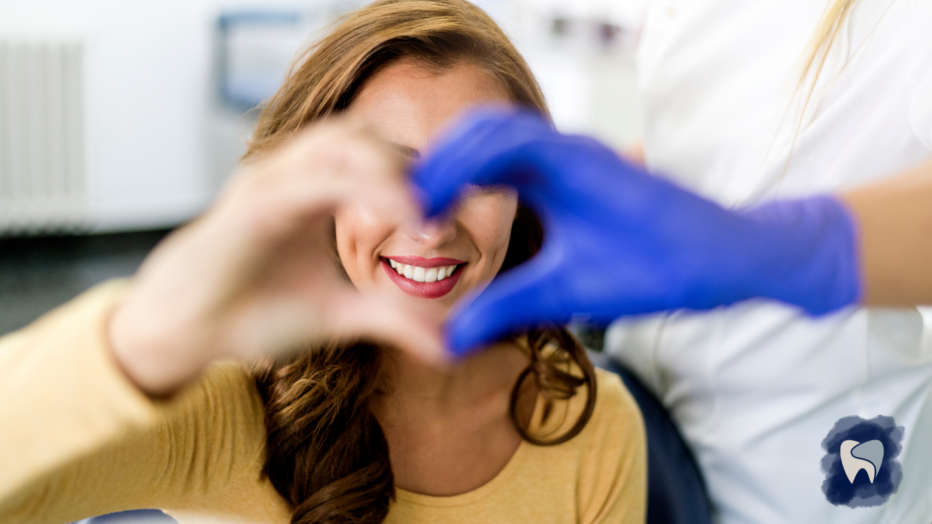 Smiling person with hands forming a heart, dental worker wearing blue gloves.