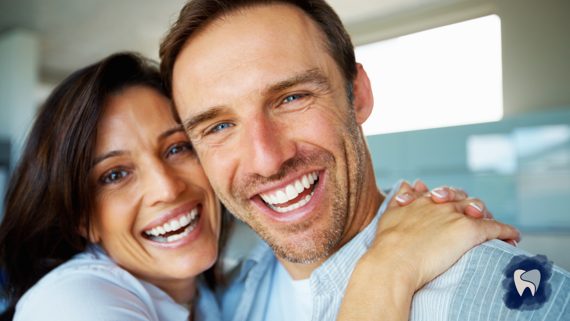 Smiling couple embracing. White teeth, indoor setting, cheerful expressions, and hugging.