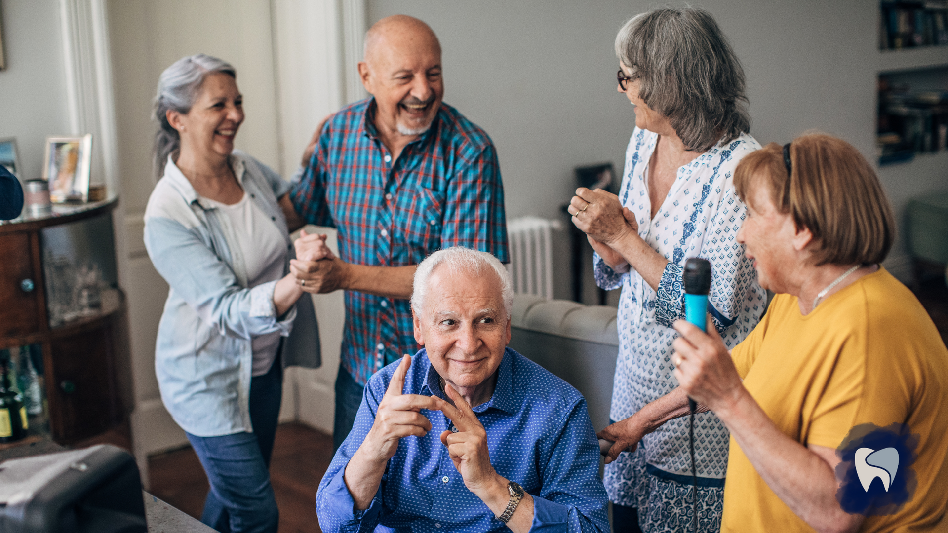 Group of older adults singing karaoke and dancing in a living room, laughing.