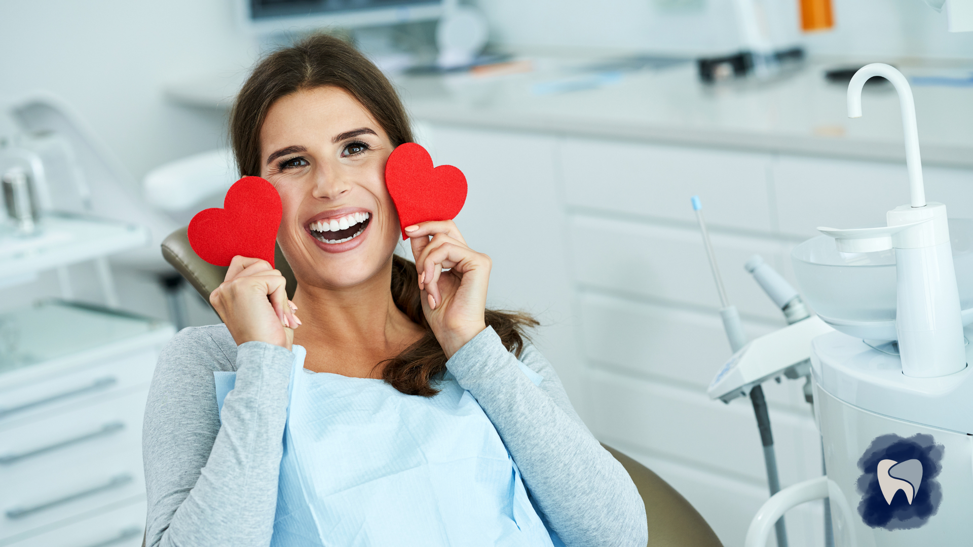 Woman in dental chair holds two red heart cutouts, smiling.