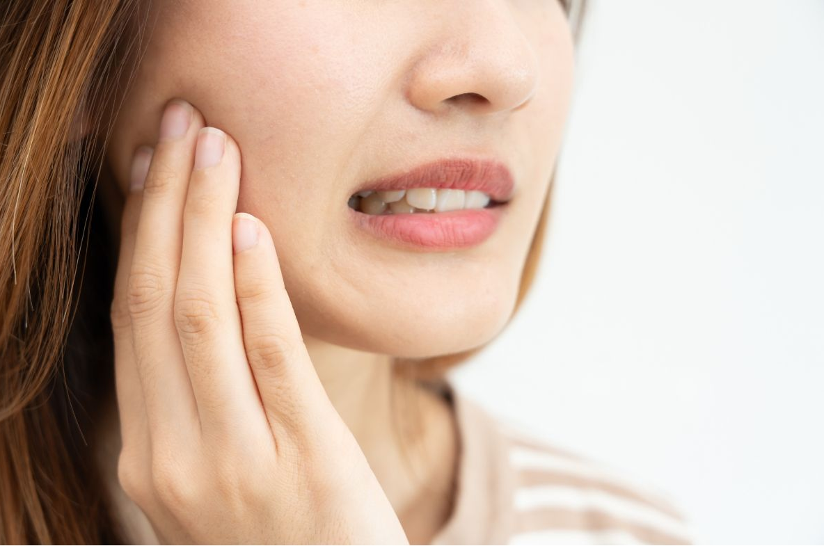 Woman with her hand on her cheek, showing pain. Brown hair, neutral background.