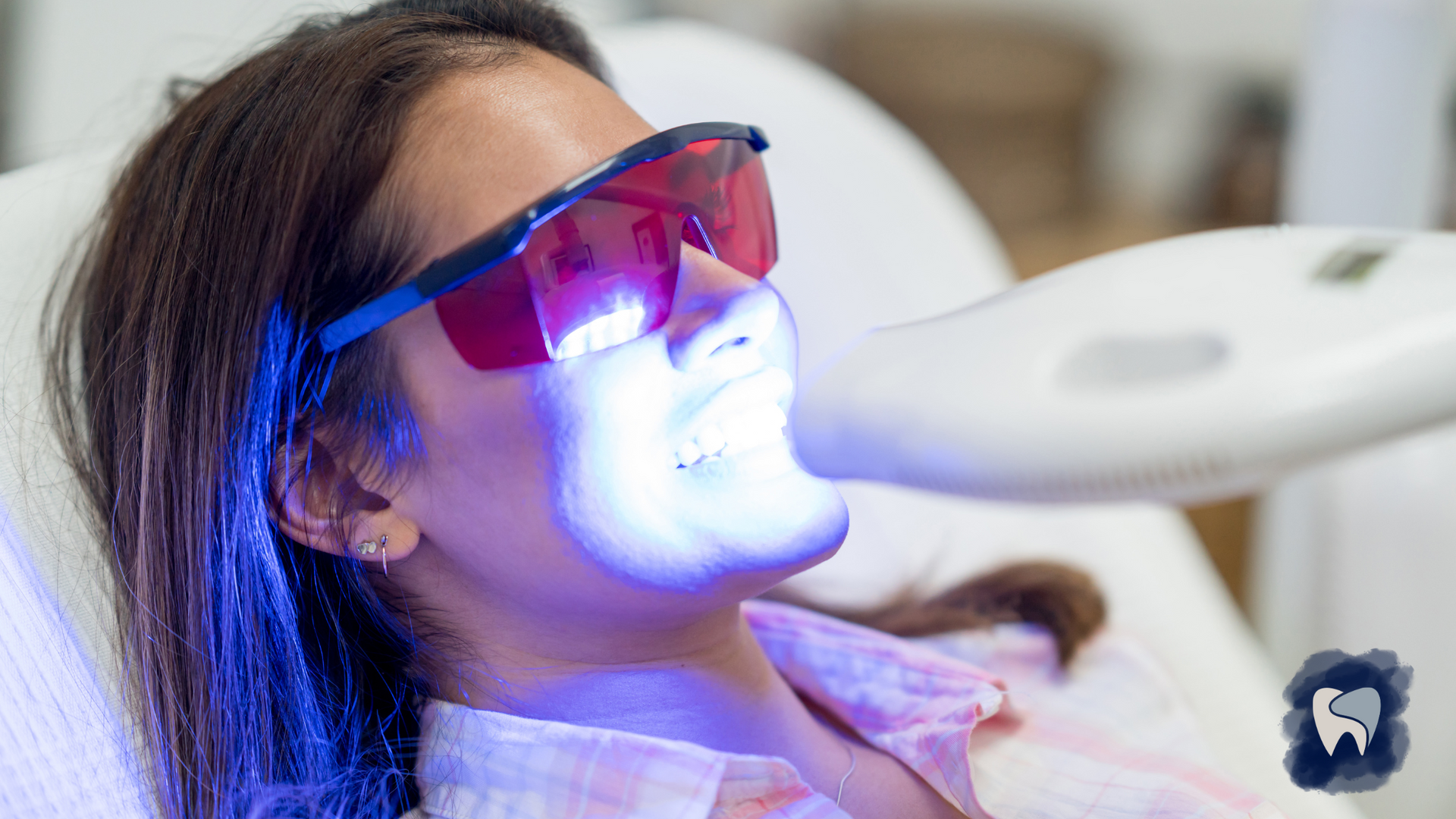 Woman undergoing teeth whitening with blue light, wearing protective glasses.