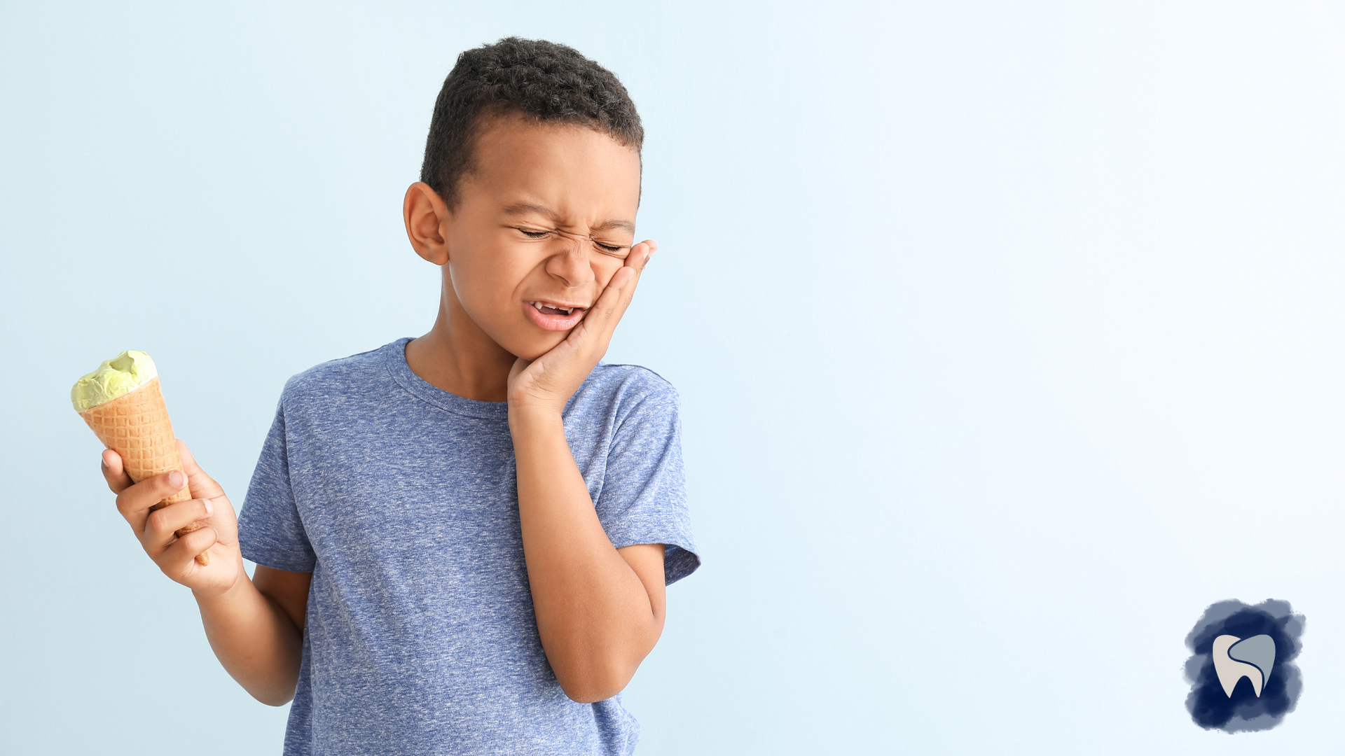 Boy with a grimace holds ice cream, touching cheek, possibly experiencing tooth sensitivity.