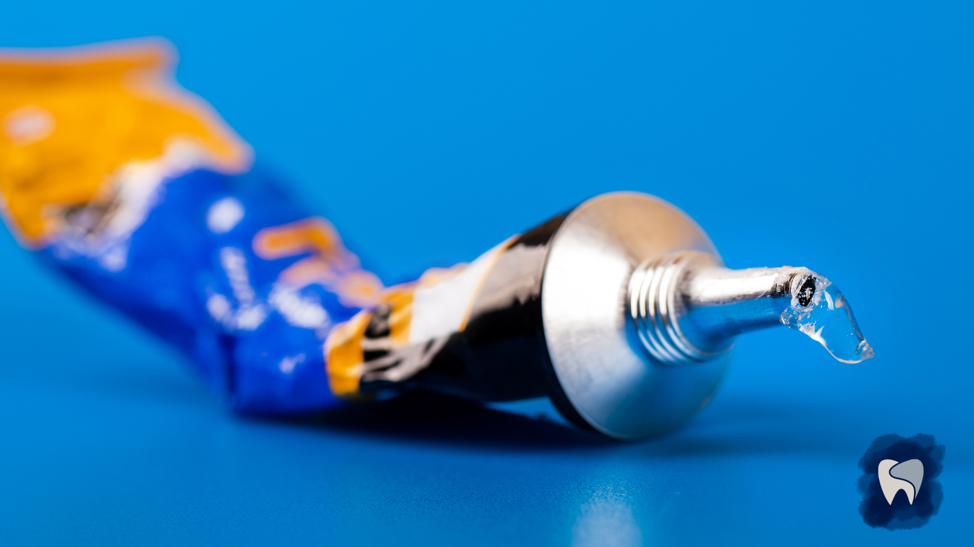 Squeezed tube of blue and yellow glue on a blue surface, with a drop of glue at the tip.