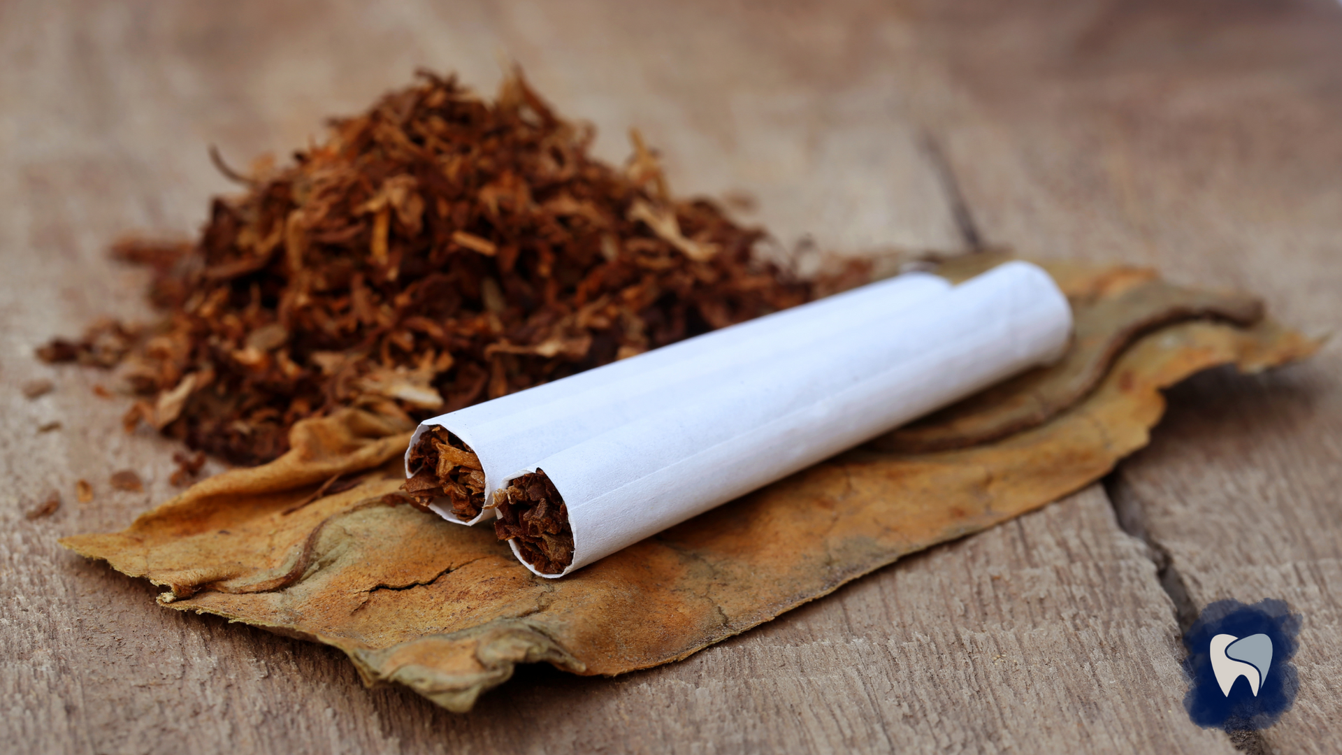 Pile of tobacco with two rolled cigarettes on a wooden surface.