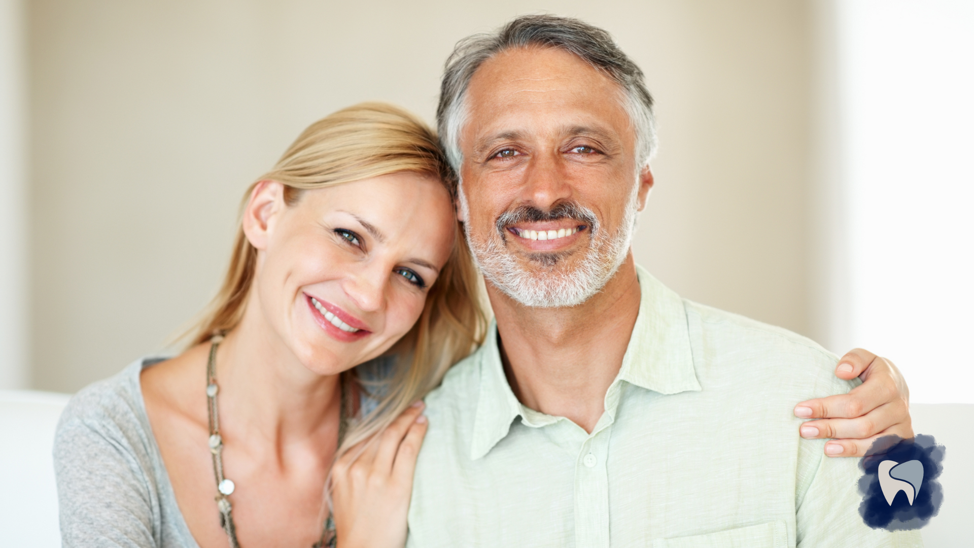 Woman and man smiling, close together. Man has arm around woman. They are indoors.