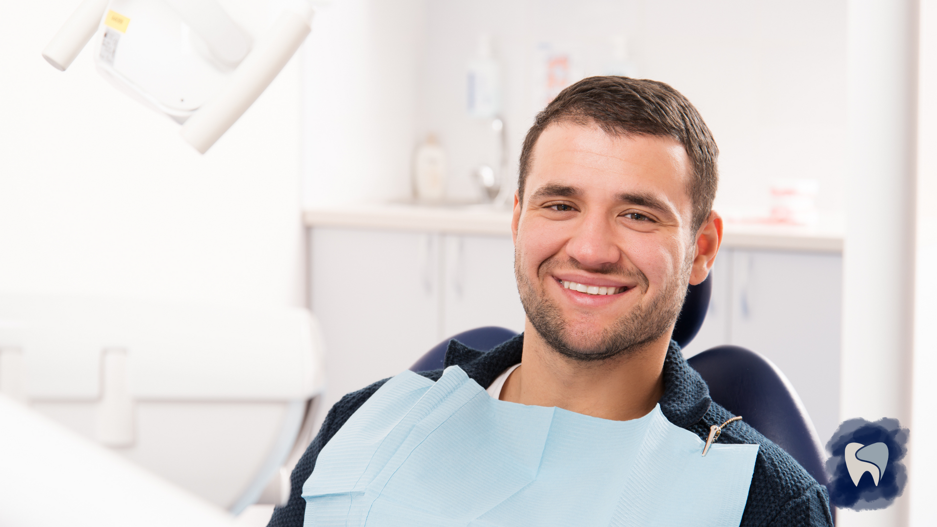 Man smiling in a dental chair, wearing a bib, in a bright dental office.