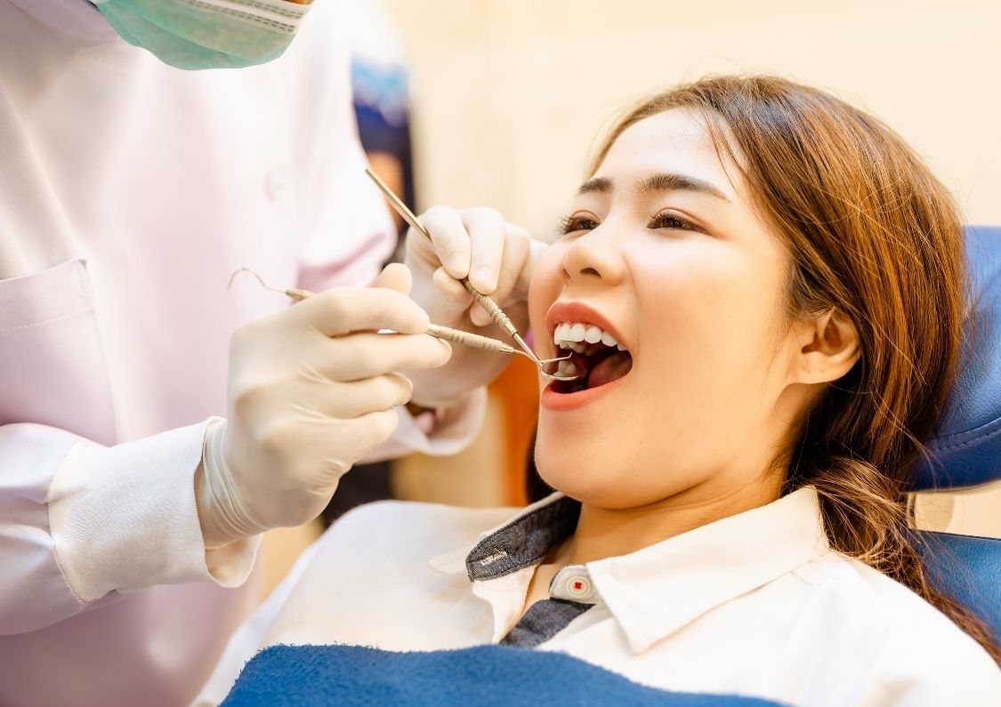 Woman at dentist, mouth open, being examined. Dentist in gloves, mask, and white coat.