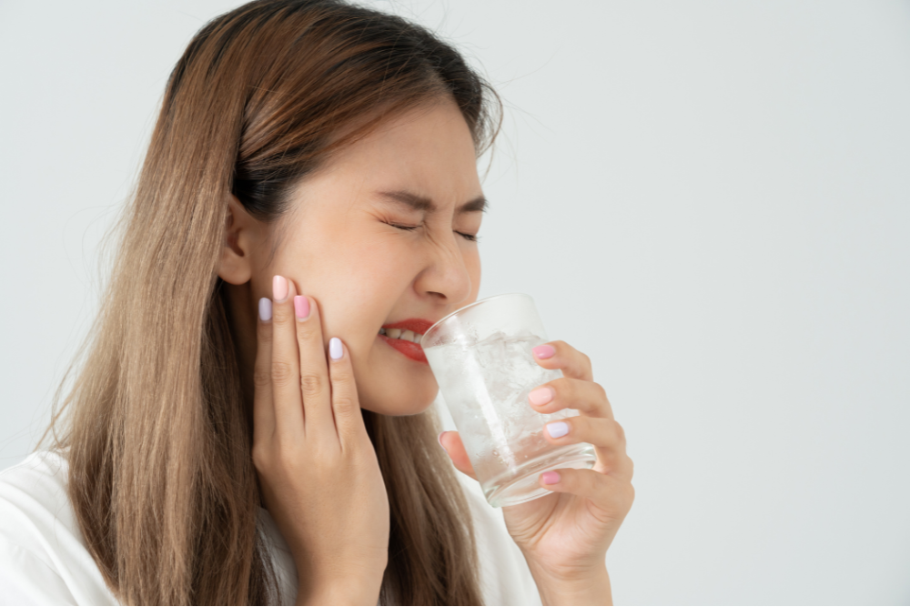 Woman with sensitive teeth grimaces while drinking cold water, holding her jaw.