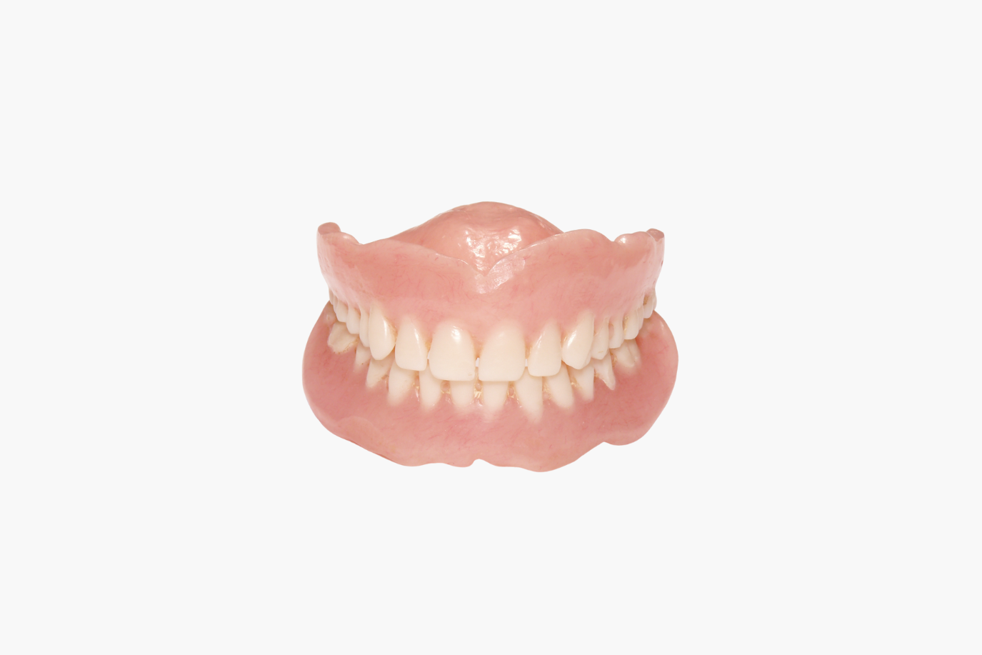 Full set of dentures, pink gum base with a row of white teeth, against a white background.