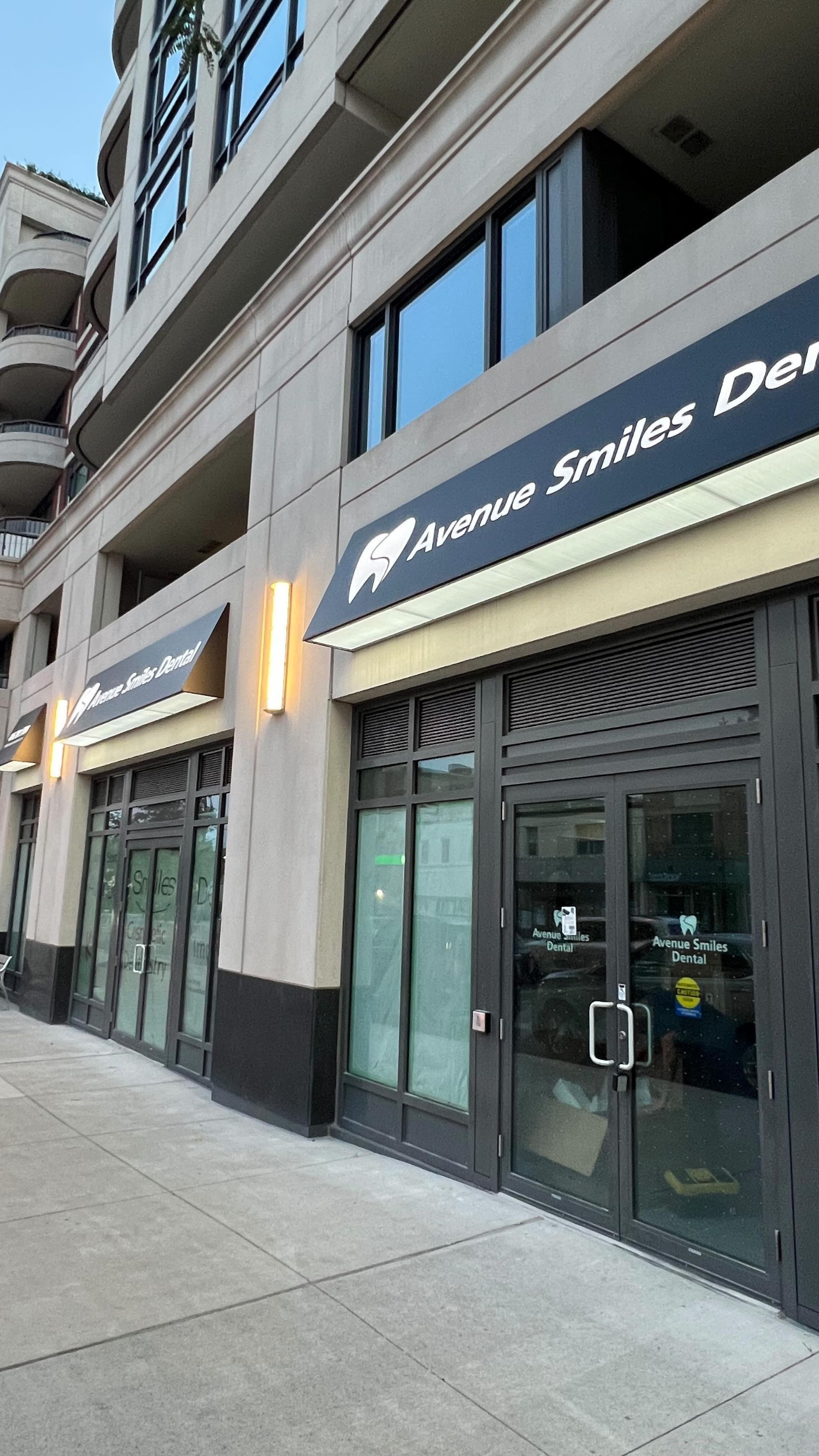 Avenue Smiles Dental office with awning on a light brown building; glass doors, street view.