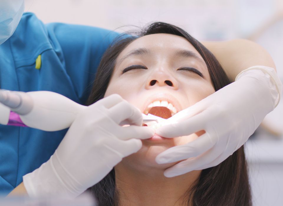 A dentist cleaning a patient's teeth. The patient is in a dental chair, mouth open.