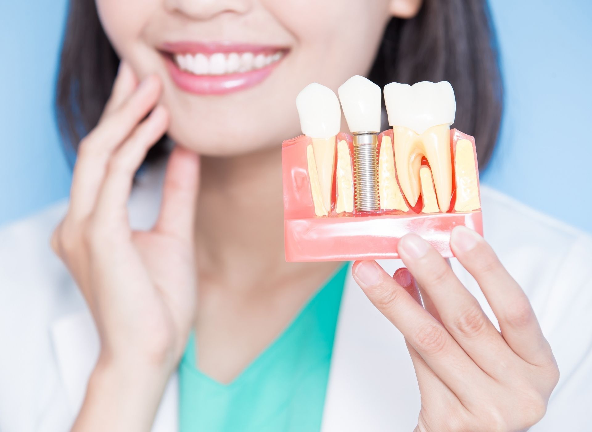 Woman holding model showing dental implant with a smiling expression.