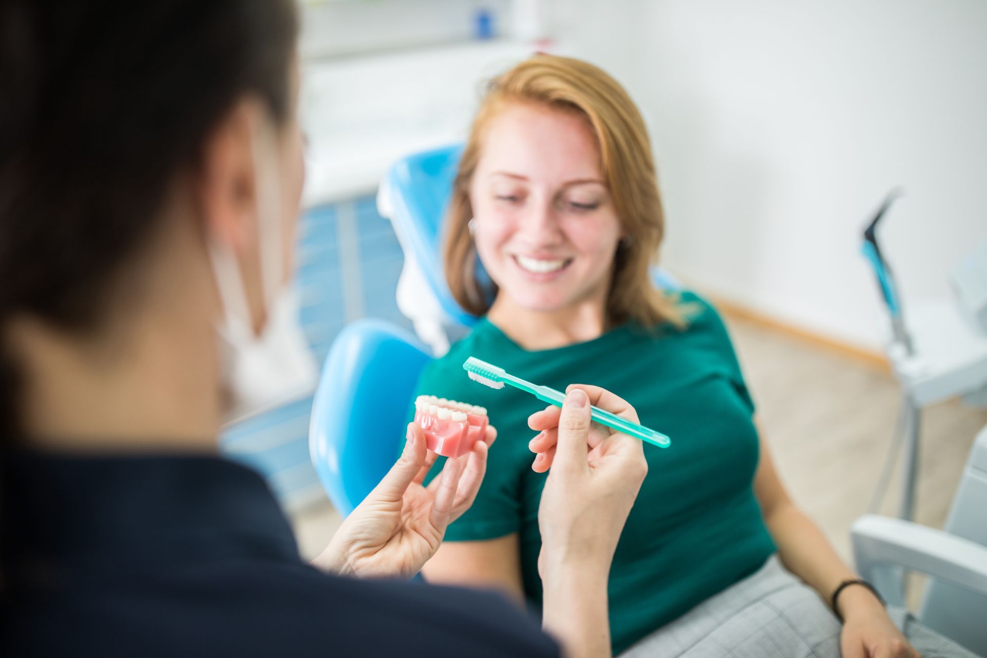 A woman is sitting in a dental chair while a dentist shows her how to brush her teeth.