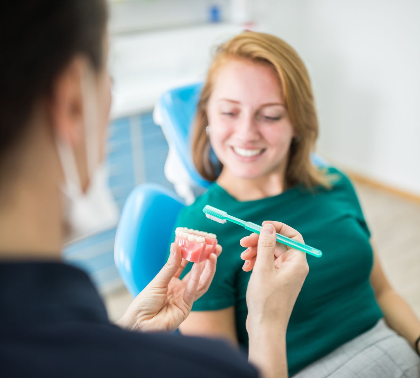 A woman is sitting in a dental chair while a dentist shows her how to brush her teeth.
