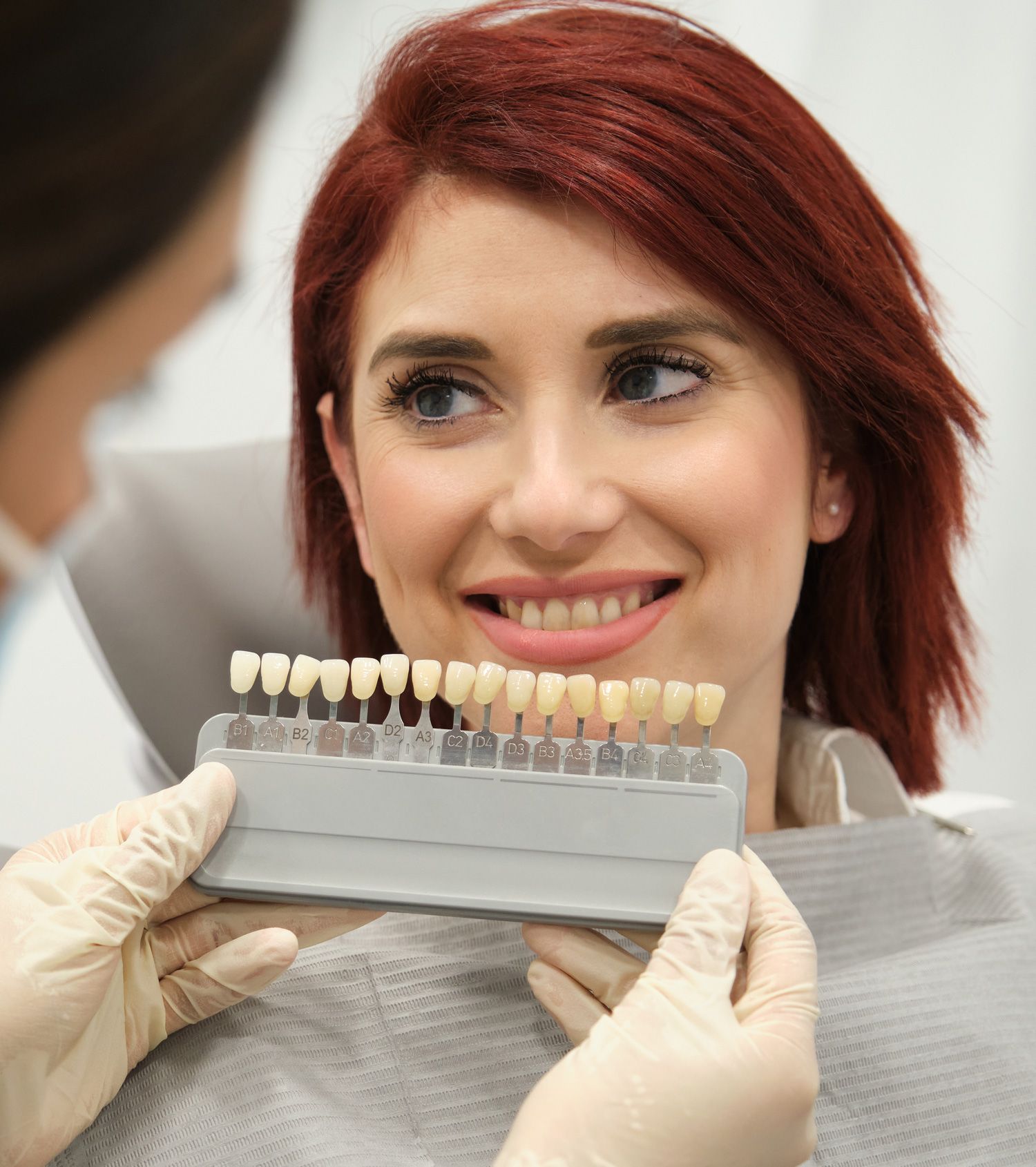 Dentist is comparing patient's teeth color with samples for whitening procedure in dental clinic.