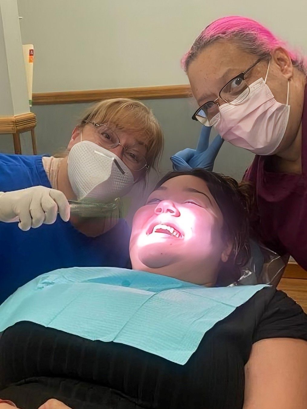 A woman is sitting in a dental chair while a dentist examines her teeth.
