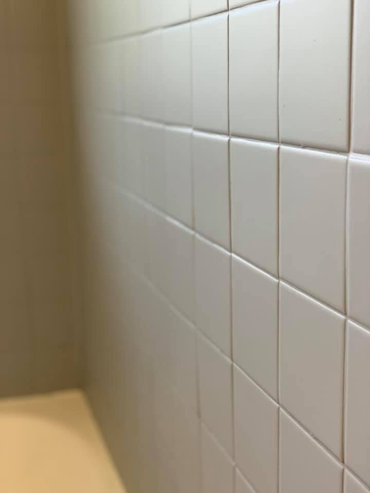 White tiled shower wall with beige walls and edge of a tub.