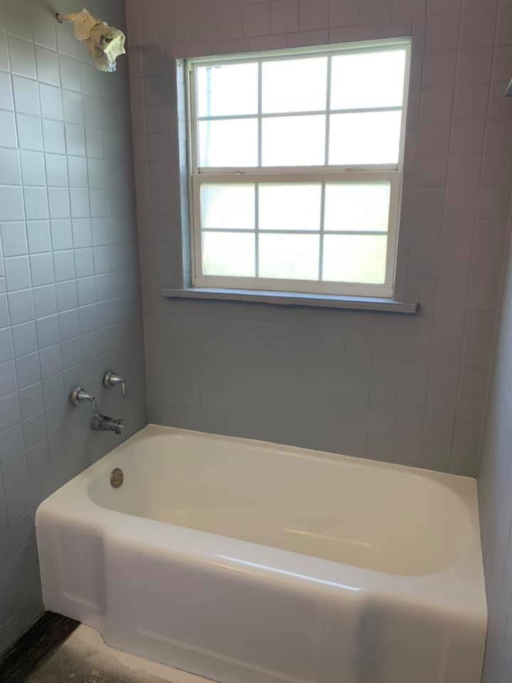 Bathroom with white tub, gray tiled walls, window, and chrome fixtures.