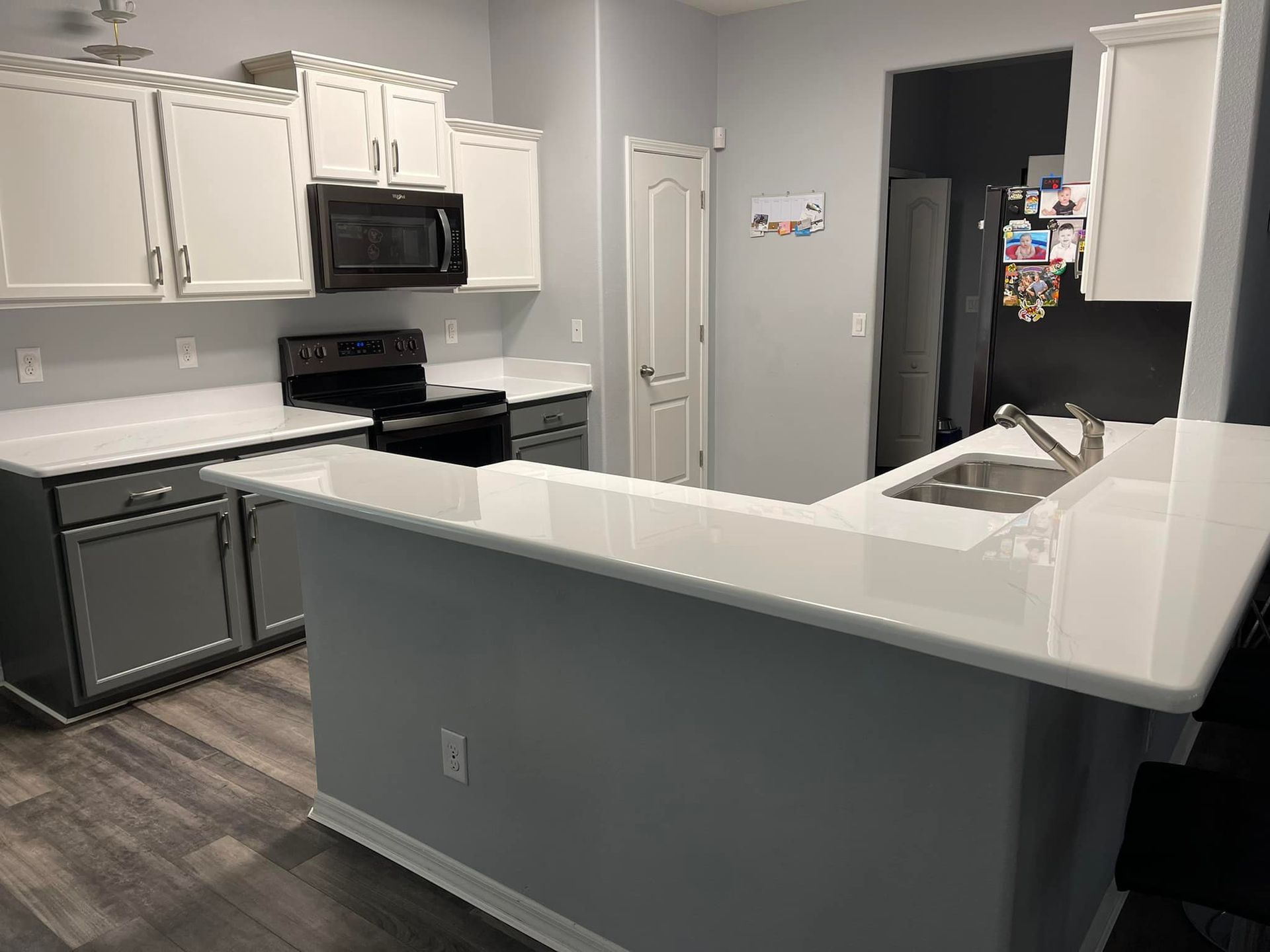 Gray and white kitchen with countertops, cabinets, and appliances; a bar area and a door.
