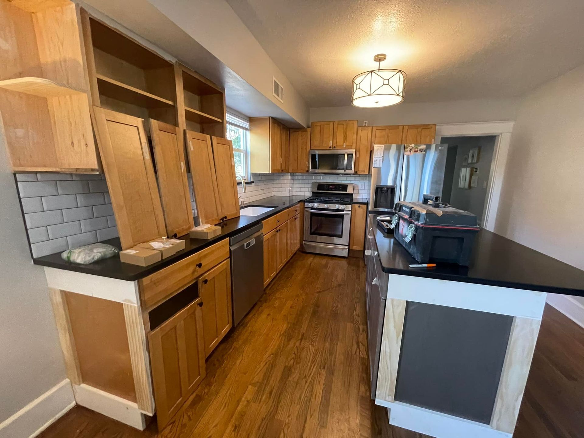 Kitchen under renovation with wooden cabinets, black countertops, and stainless steel appliances.