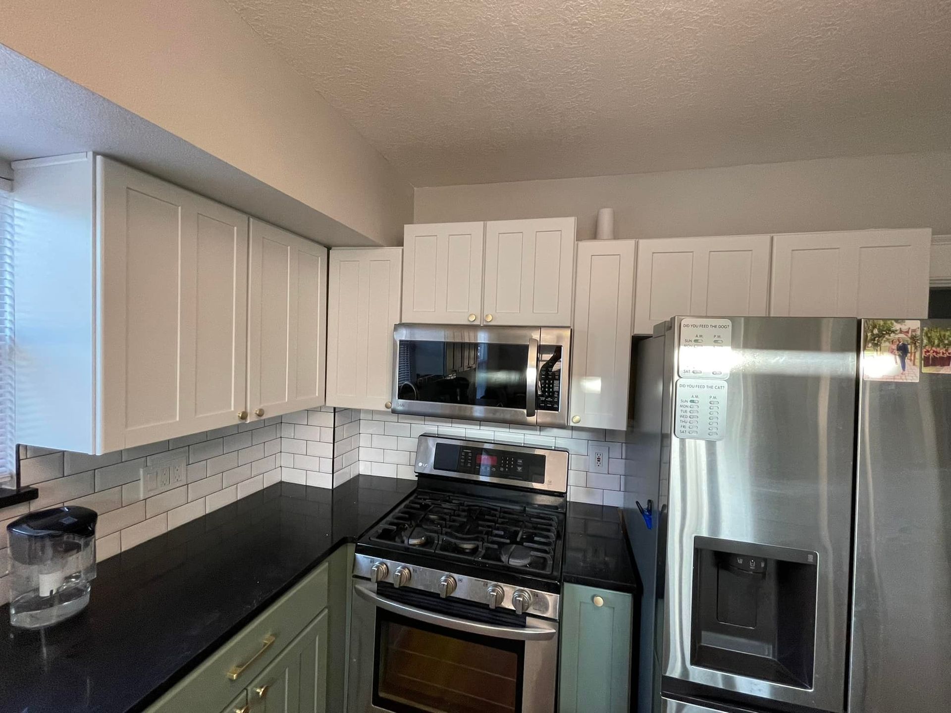 White kitchen cabinets, stainless steel appliances, black countertop, and green lower cabinets.