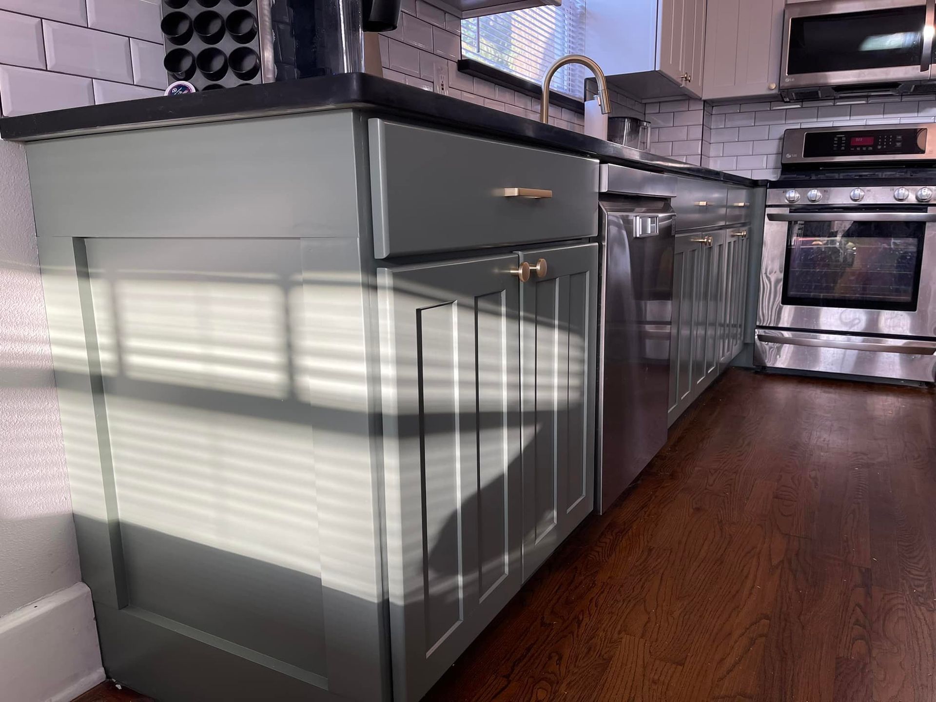 Green kitchen cabinets with gold hardware. Stainless steel appliances and dark wood floors.