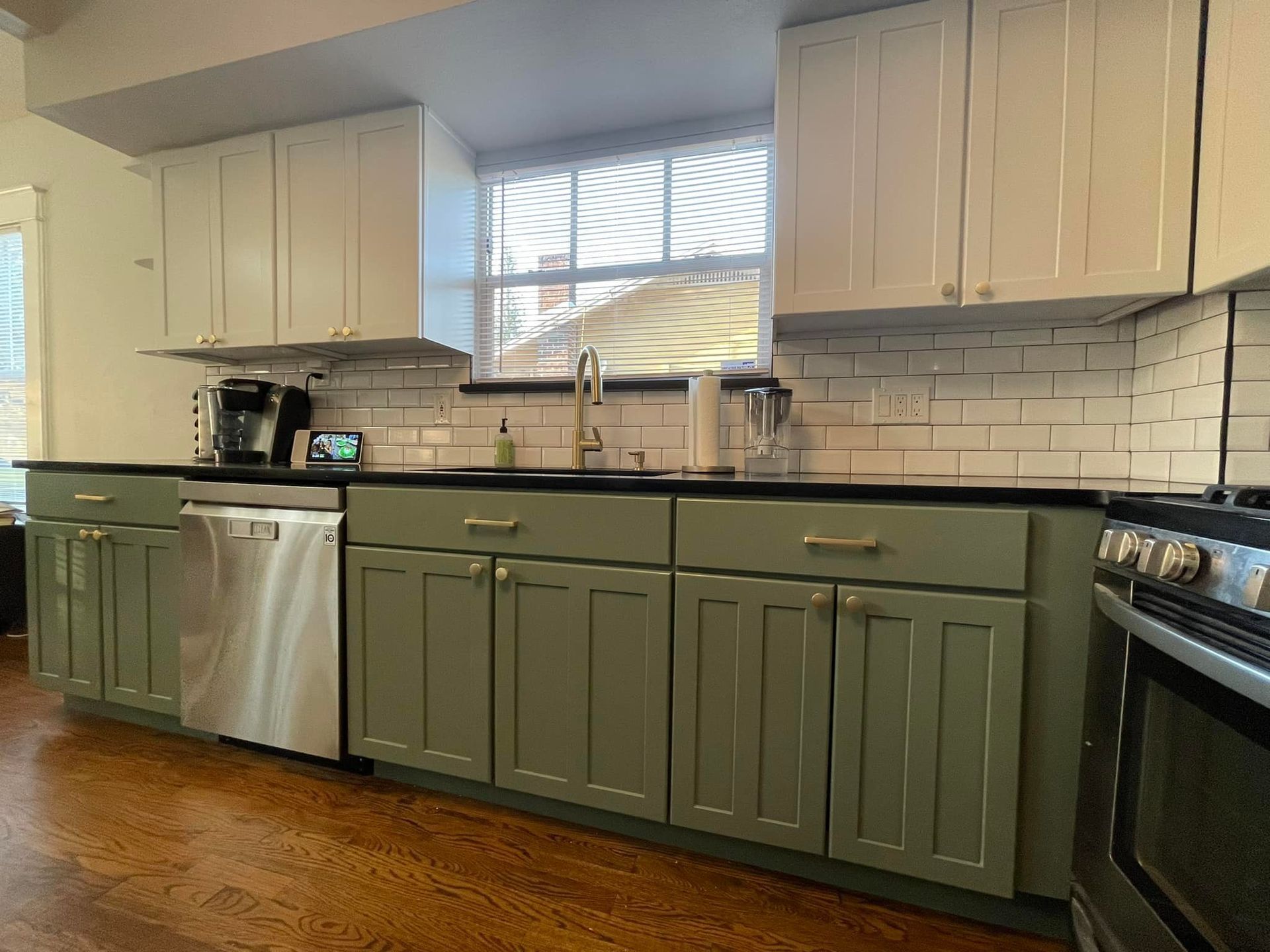 Kitchen with sage green lower cabinets, white upper cabinets, stainless steel appliances, and a window.